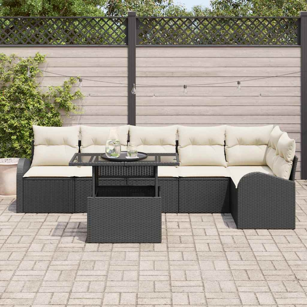 Juego de patio al aire libre con muebles de mimbre gris, cojines beige y una mesa con tapa de cristal. El fondo tiene una valla de madera y vegetación.