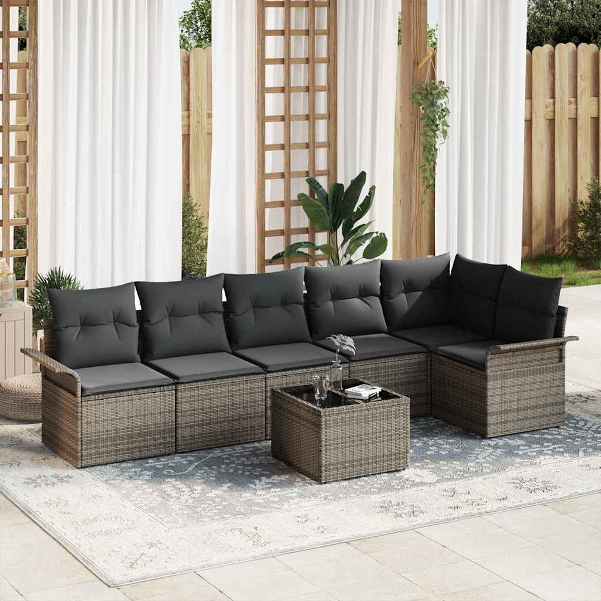 Outdoor-Ecksofa mit grauen Kissen und passendem Couchtisch. Weiße Vorhänge und Holzzaun im Hintergrund.
