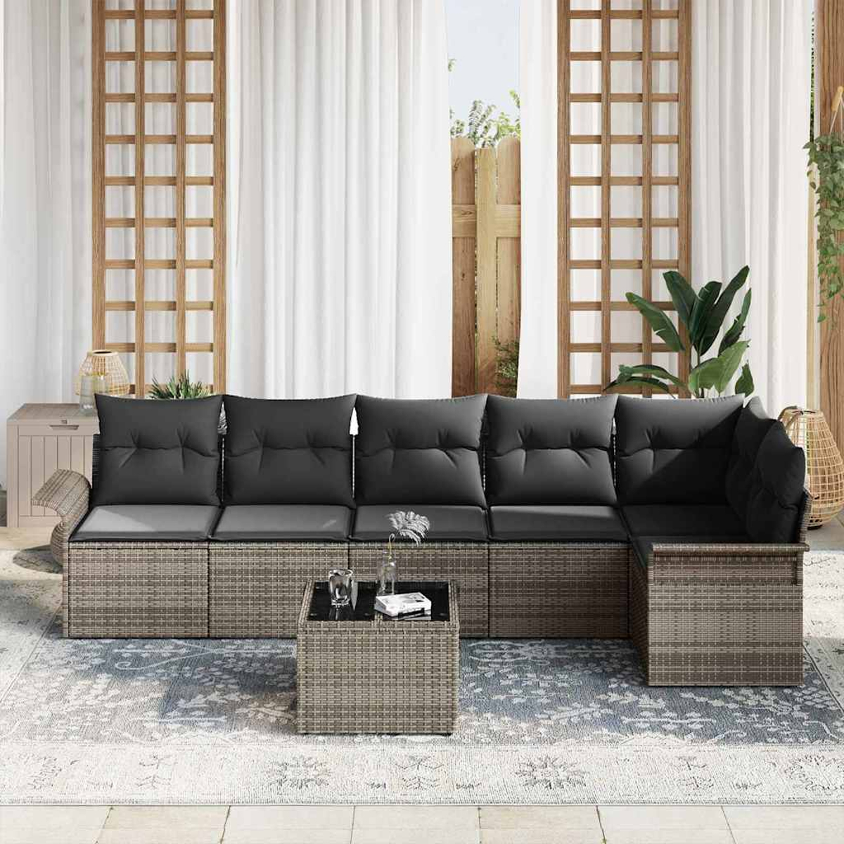 Ein Outdoor-Wicker-Ecksofa mit schwarzen Kissen, einem kleinen Tisch und einem Teppich. Vorhänge und ein Gitterfenster sind im Hintergrund.