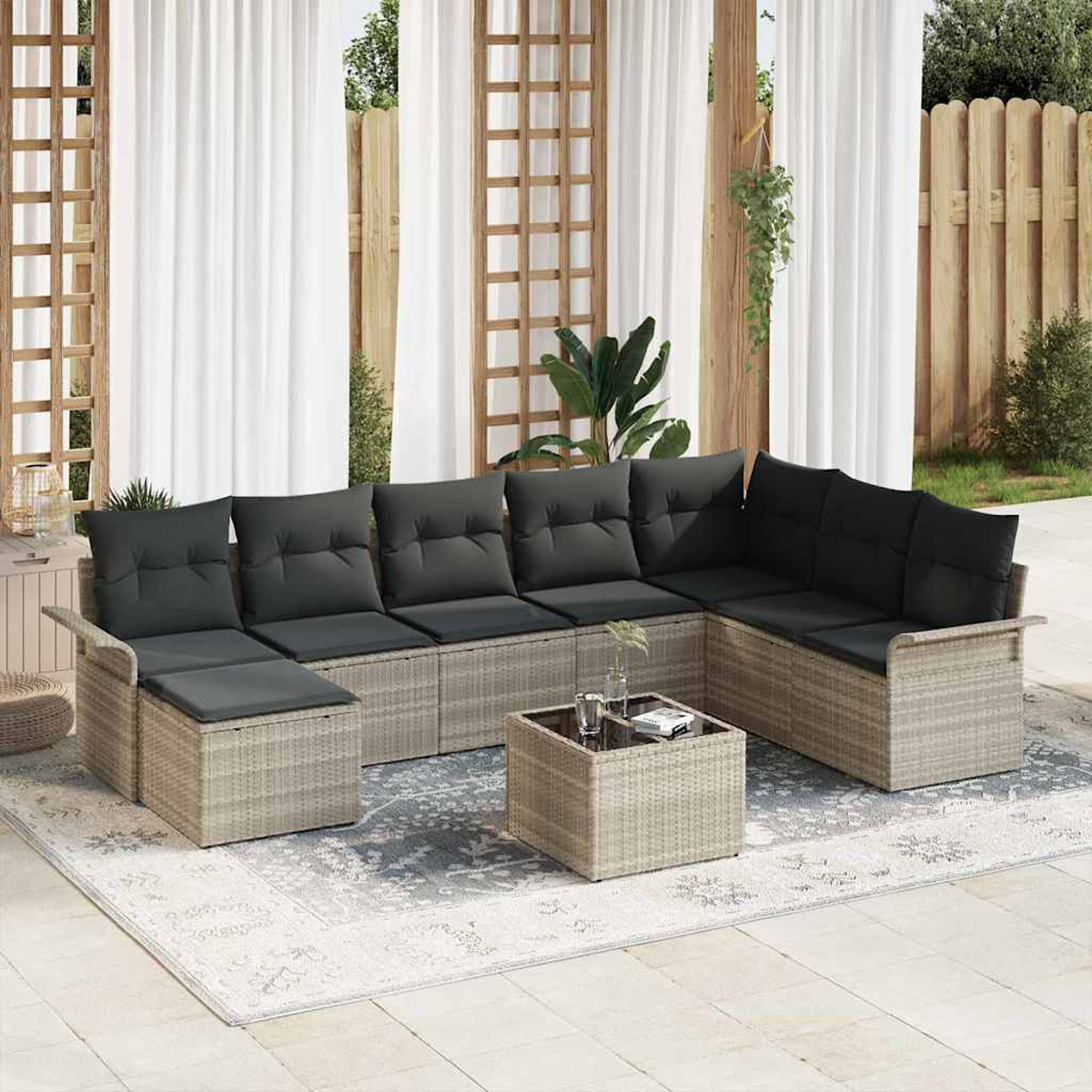 Outdoor-Ecksofa mit grauen Kissen und einem kleinen Tisch auf einem gemusterten Teppich. Weiße Vorhänge und Holzzaun im Hintergrund.