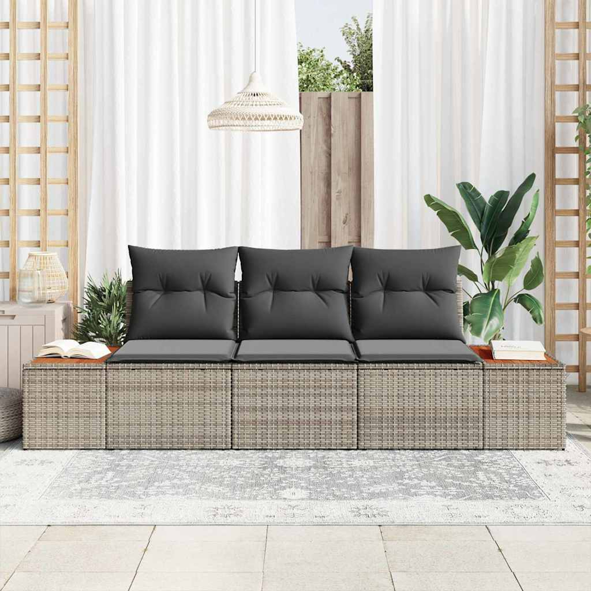 Outdoor-Sitzarrangement mit grauen Kissen, Rattan-Basis und Holztischen. Weiße Vorhänge und eine grüne Pflanze sind im Hintergrund.
