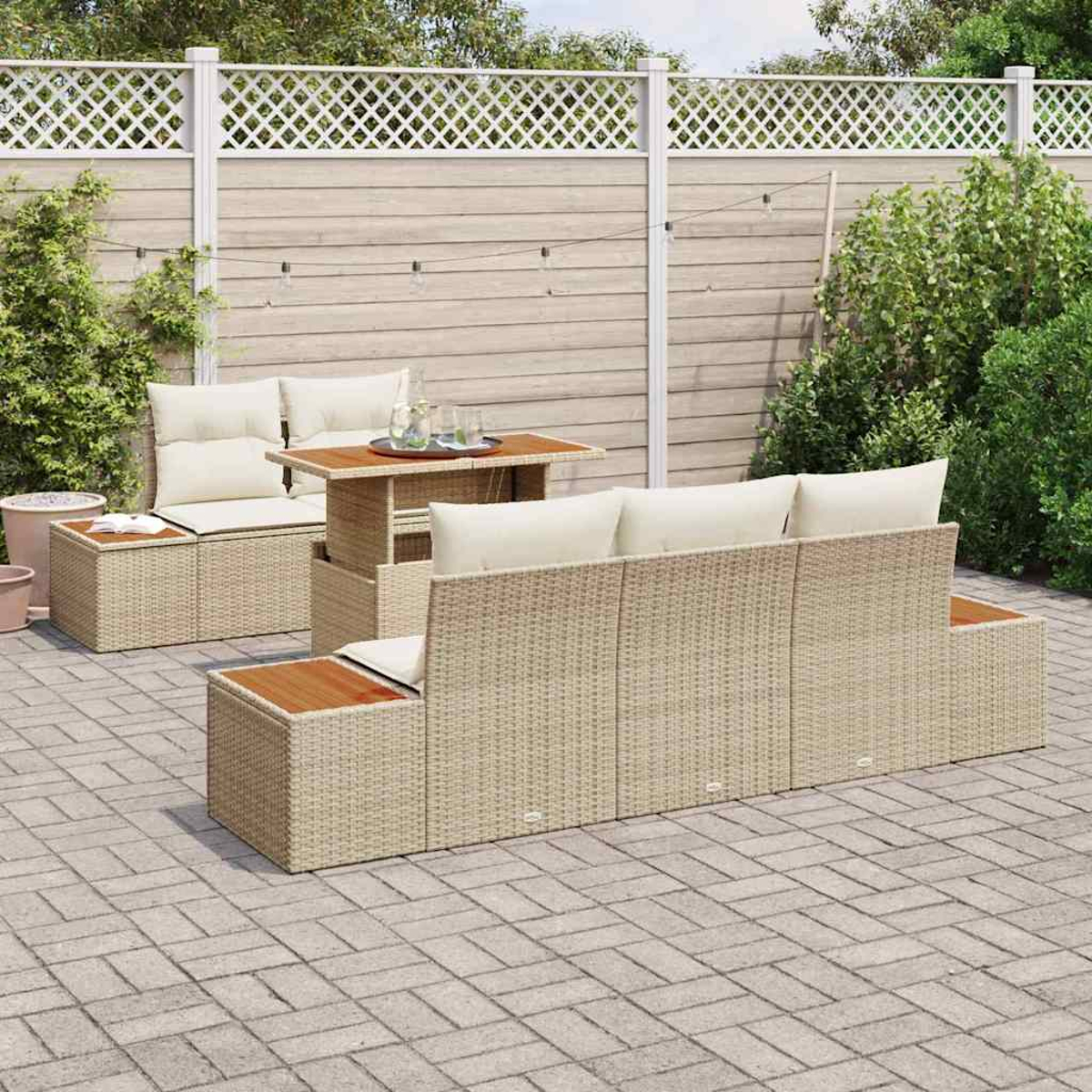 Terrassenmöbel-Set mit beigen Korbmöbeln, bestehend aus Sofa, zwei Ottomanen und einem Tisch, auf einer Ziegelpflasterung mit Holzzaun.