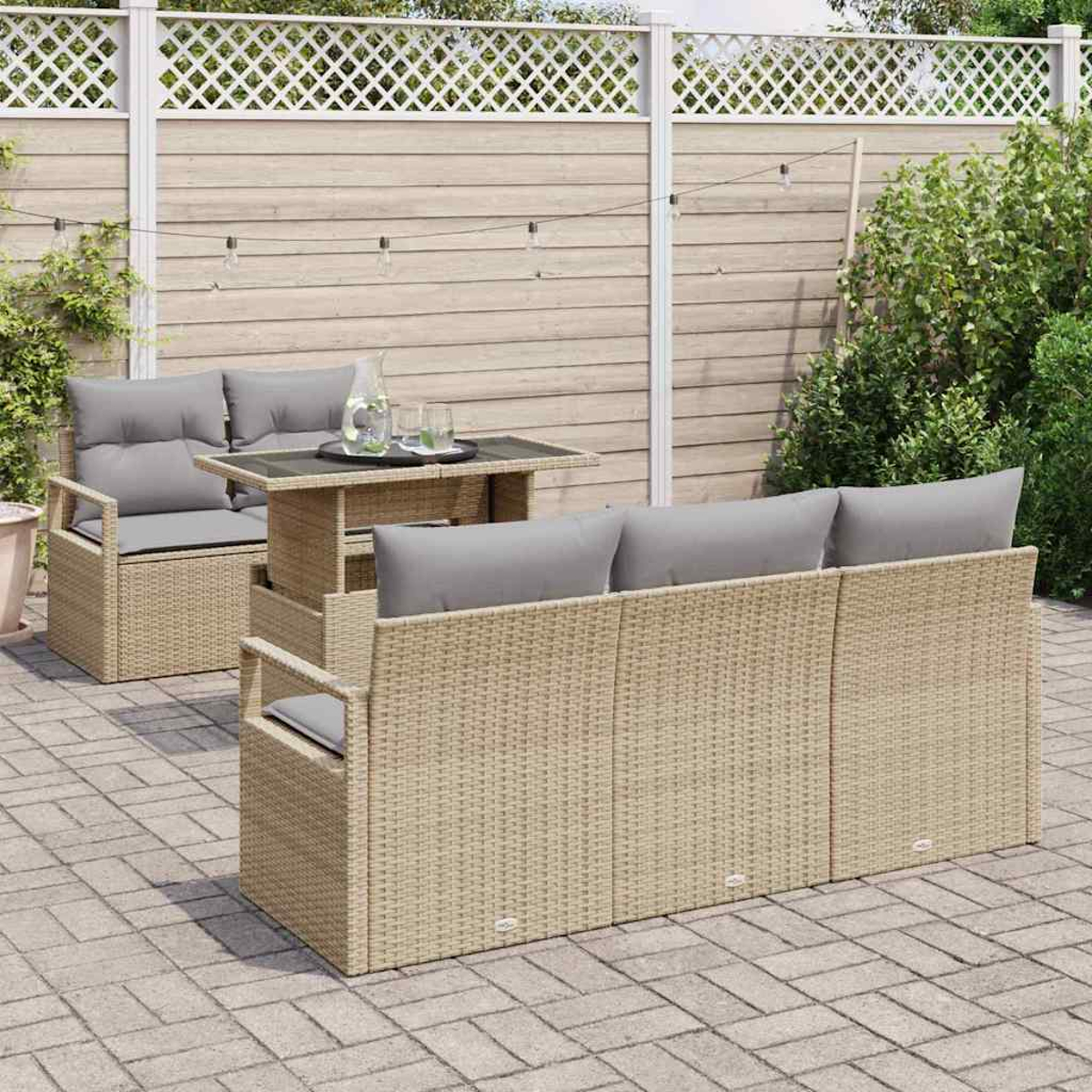 Juego de muebles de mimbre para exterior: sofá, sofá de dos plazas y mesa con cojines grises. Fondo con valla de madera y plantas.