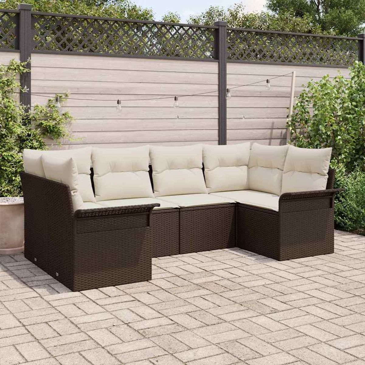 Ein Ecksofa mit cremefarbenen Kissen steht auf einer Ziegelstein-Terrasse. Im Hintergrund ein Holzzaun und Grün.