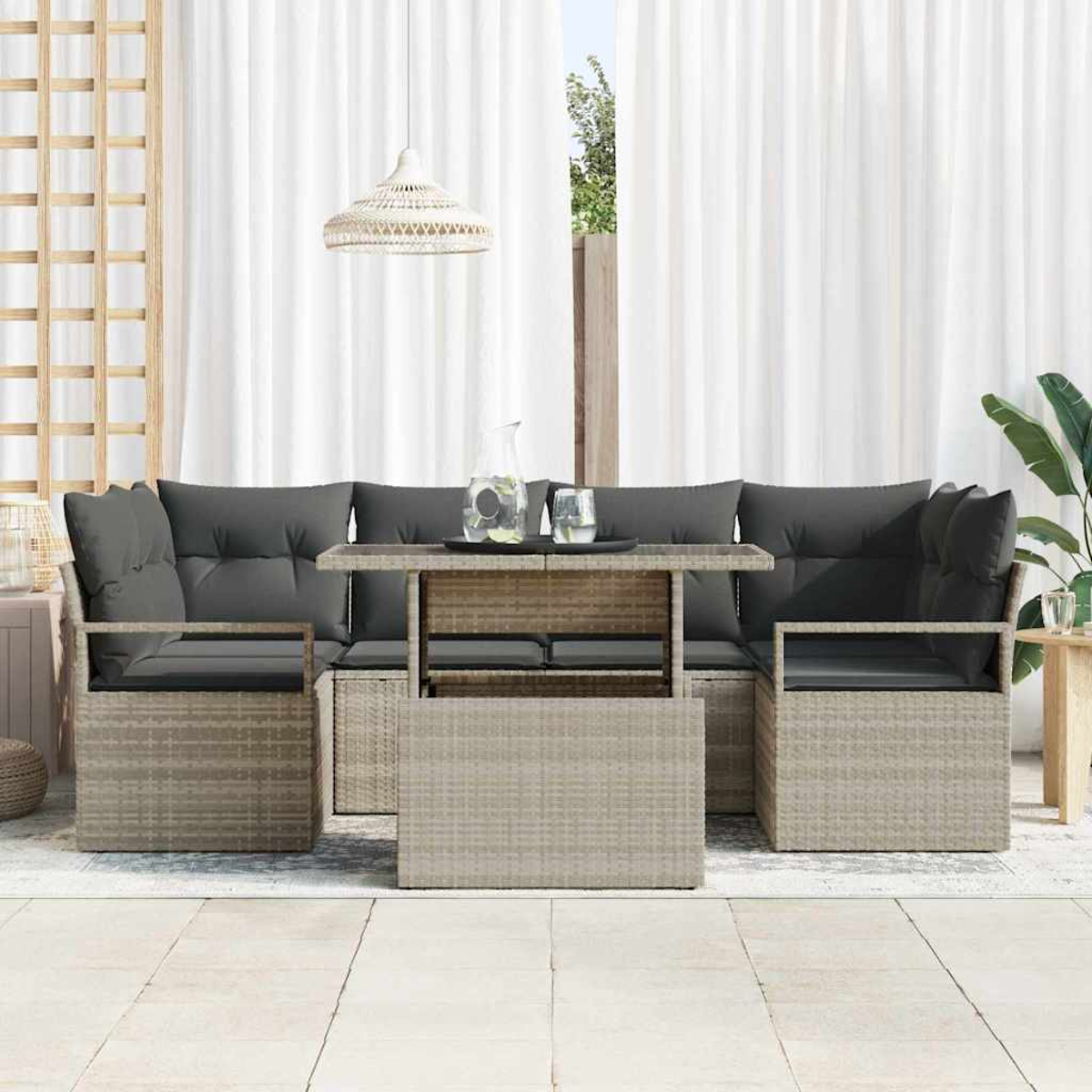 Gartenmöbel-Set mit Tisch und Sitzgelegenheiten. Graue Kissen auf gewebten Stühlen. Weiße Vorhänge und eine Hängeleuchte.