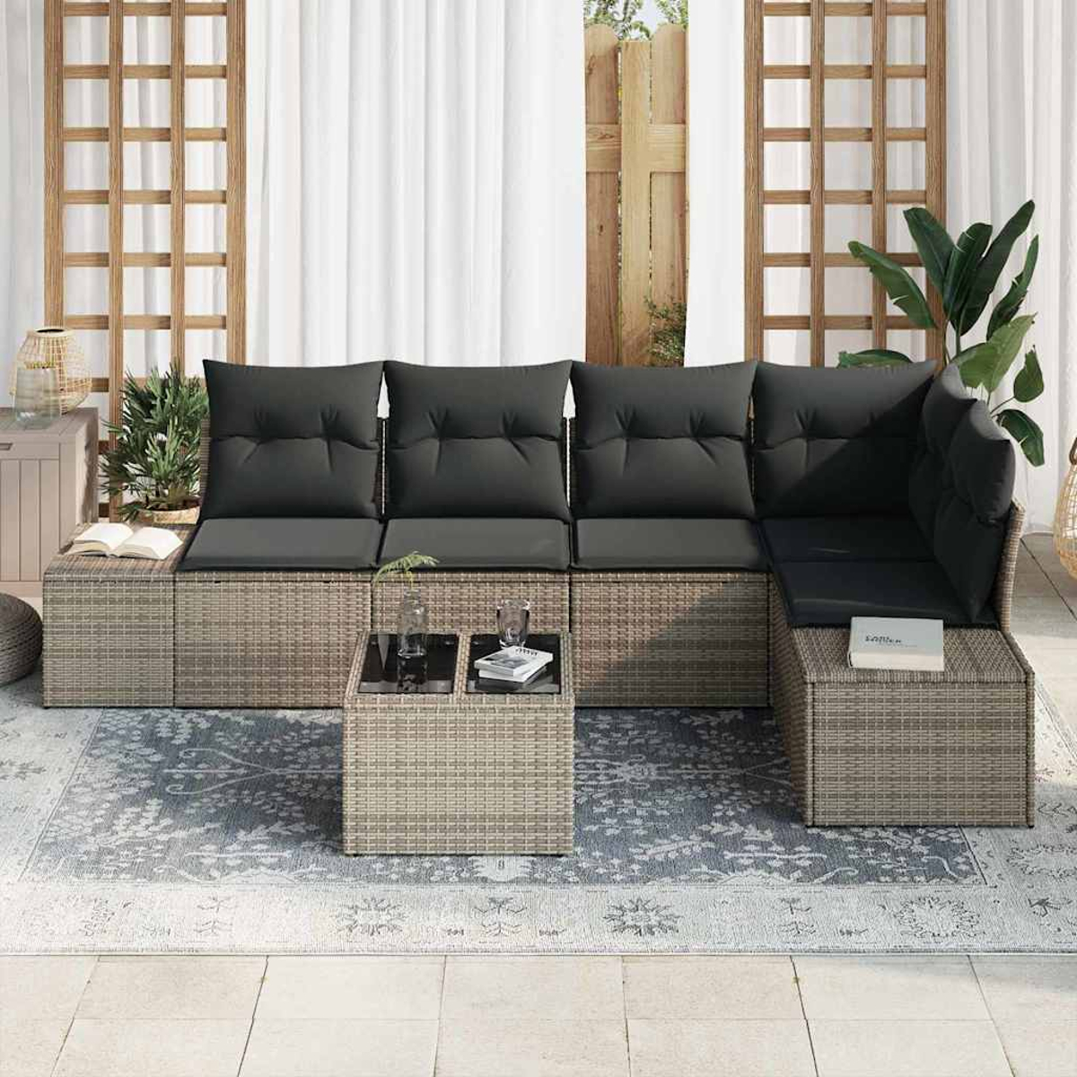 Outdoor-Ecksofa mit grauen Kissen, kleinem Tisch, Teppich und Pflanzen. Im Hintergrund Vorhänge und Holzgitter.