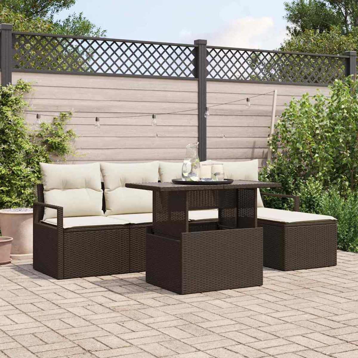 Terrassenset mit braunen Korbmöbeln, cremefarbenen Kissen und einem Tisch. Dahinter ein Gitterzaun und Pflanzen.