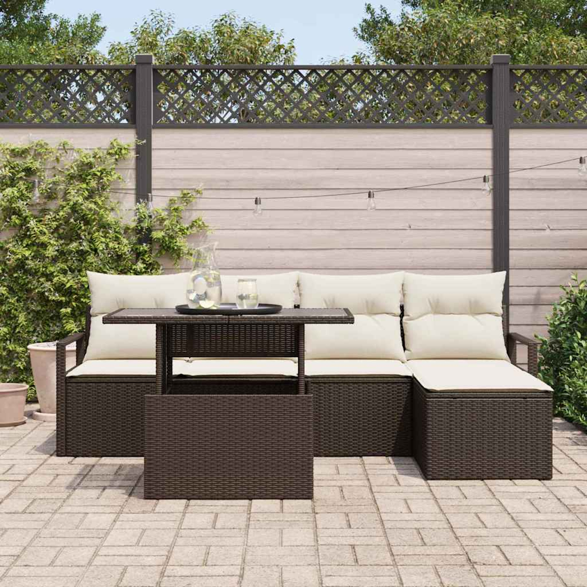 Outdoor-Terrassenset mit braunen Korbmöbeln, cremefarbenen Kissen und einem kleinen Tisch. Im Hintergrund ein Holzzaun mit Pflanzen.
