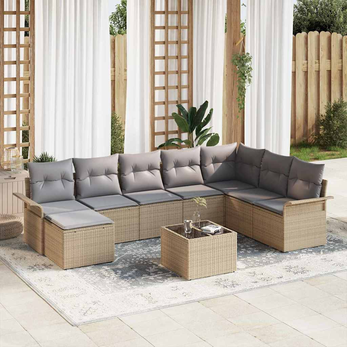 Ein Ecksofa im Freien mit grauen Kissen und einem kleinen Tisch auf einem gemusterten Teppich. Weiße Vorhänge und Holzzaun im Hintergrund.