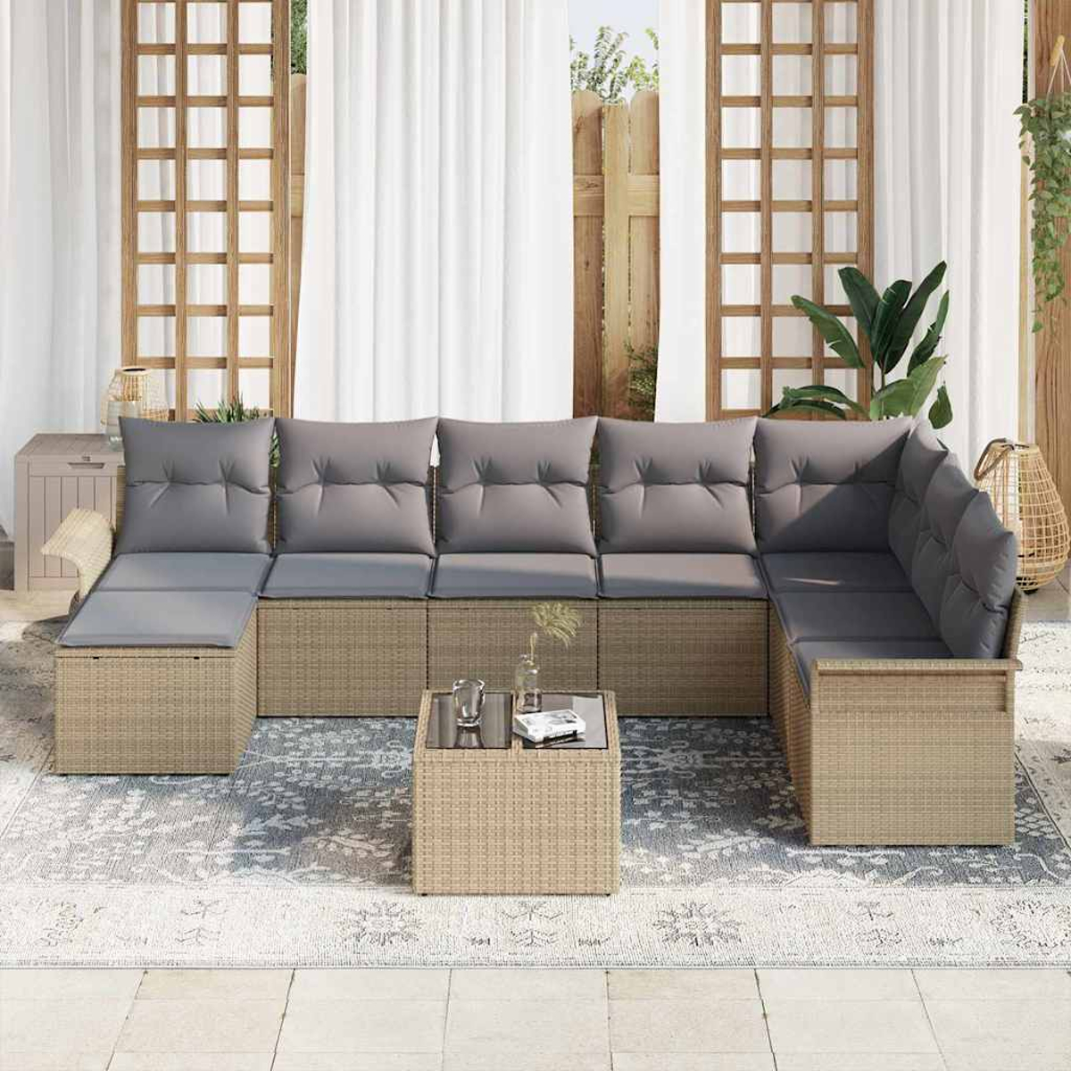 Geflochtenes Outdoor-Ecksofa mit grauen Kissen. Couchtisch, Teppich und Grün. Weiße Vorhänge, Holzgitter und eine neutrale Farbpalette.