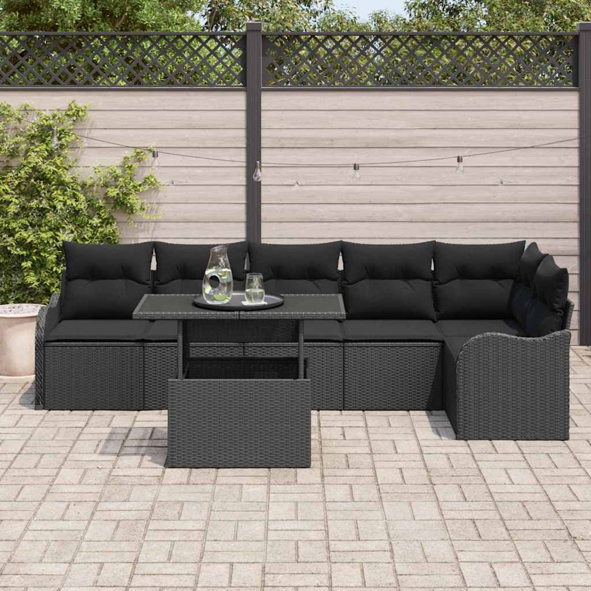 Terrassenset mit schwarzen Kissen. Enthält einen Tisch mit Glas und Wasserkrug. Vor einem Holzzaun.