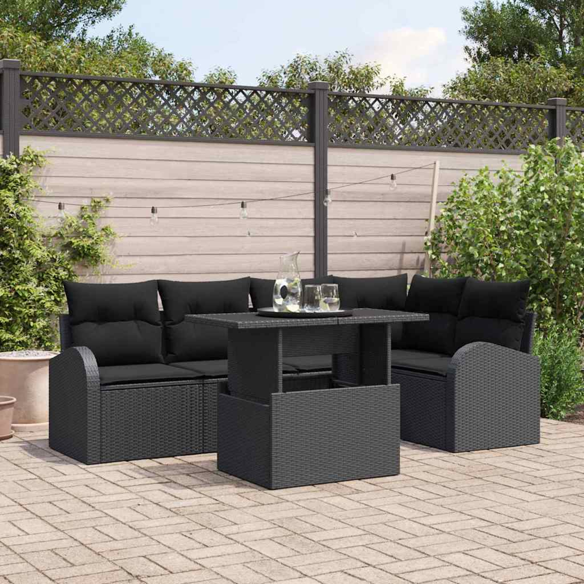 Schwarzes Outdoor-Korbmöbel-Set. Enthält einen Tisch, ein Sofa und zwei Stühle. Ein Krug und Gläser auf dem Tisch. Holzzaun im Hintergrund.