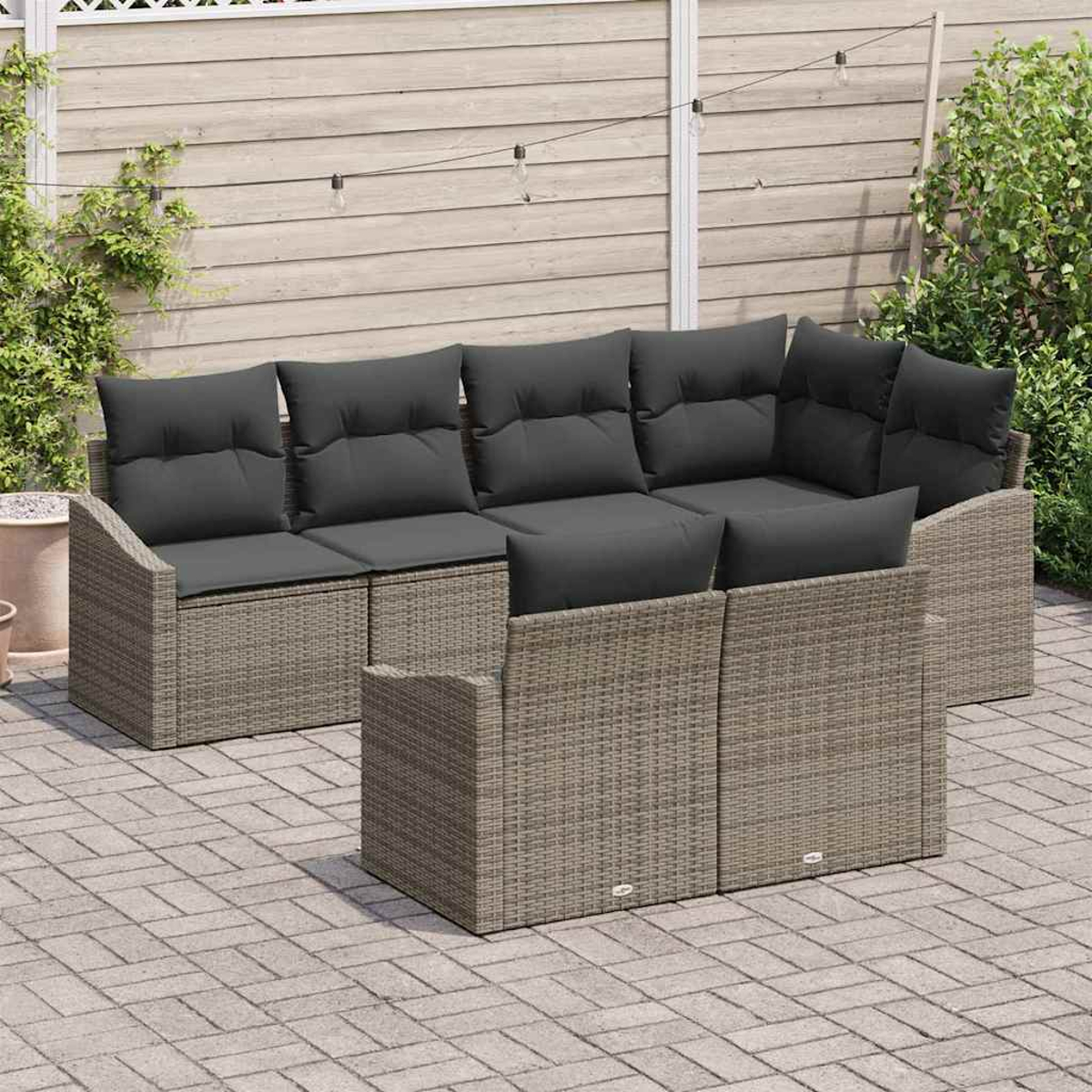 Juego de sofás de mimbre para exteriores con cojines gris oscuro en un patio. Valla de madera y plantas en el fondo.