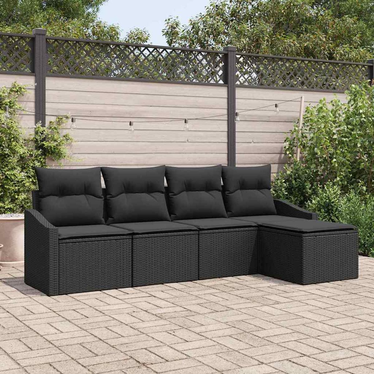 Schwarzes Korbmöbel mit Kissen auf einer Terrasse. Ein Holzzaun mit Pflanzen und Lichterketten befindet sich hinter dem Sofa.