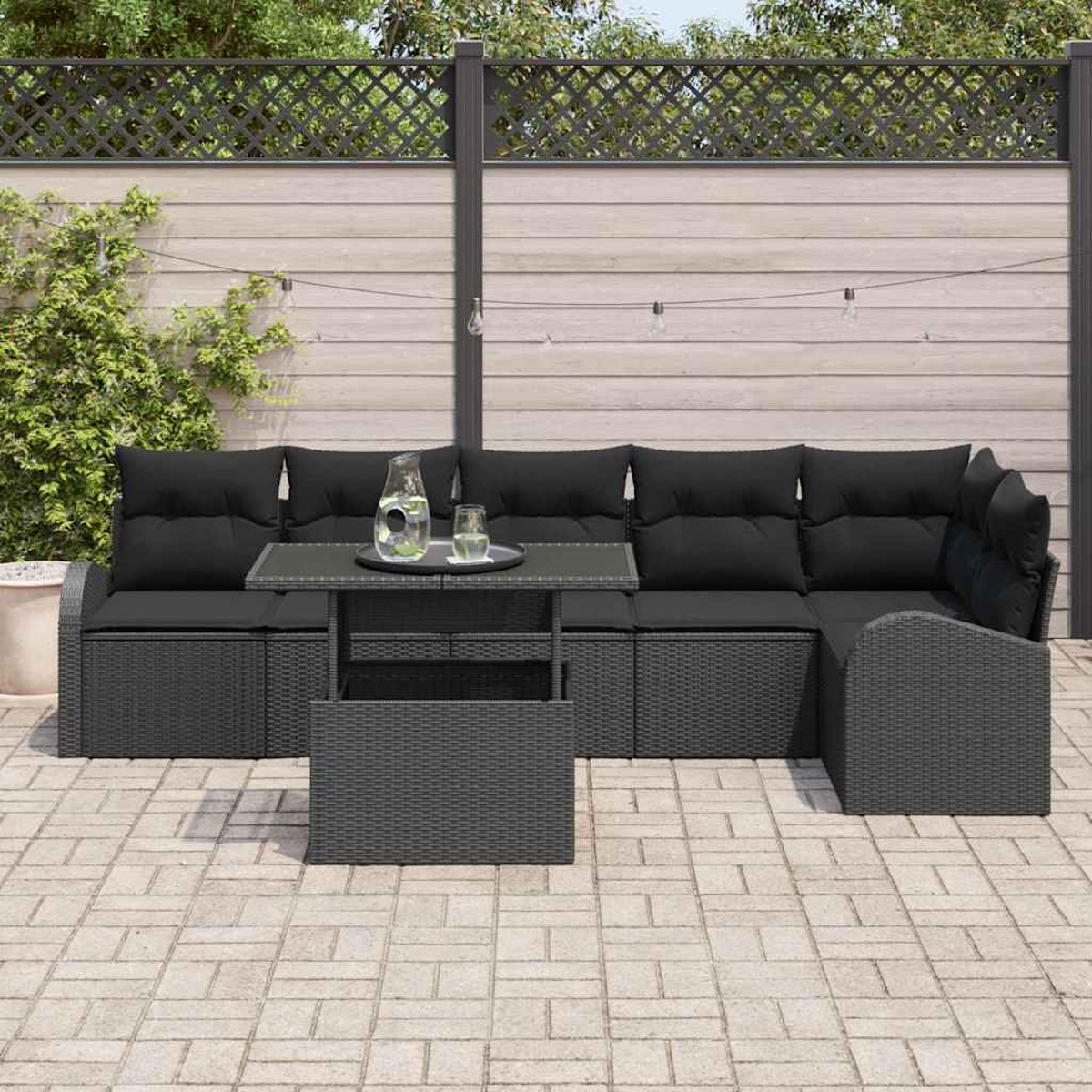 Garten-Sitzgruppe mit schwarzen Kissen und Tisch. Die Gruppe steht auf einer Backsteinterrasse, im Hintergrund Zaun und Grün.