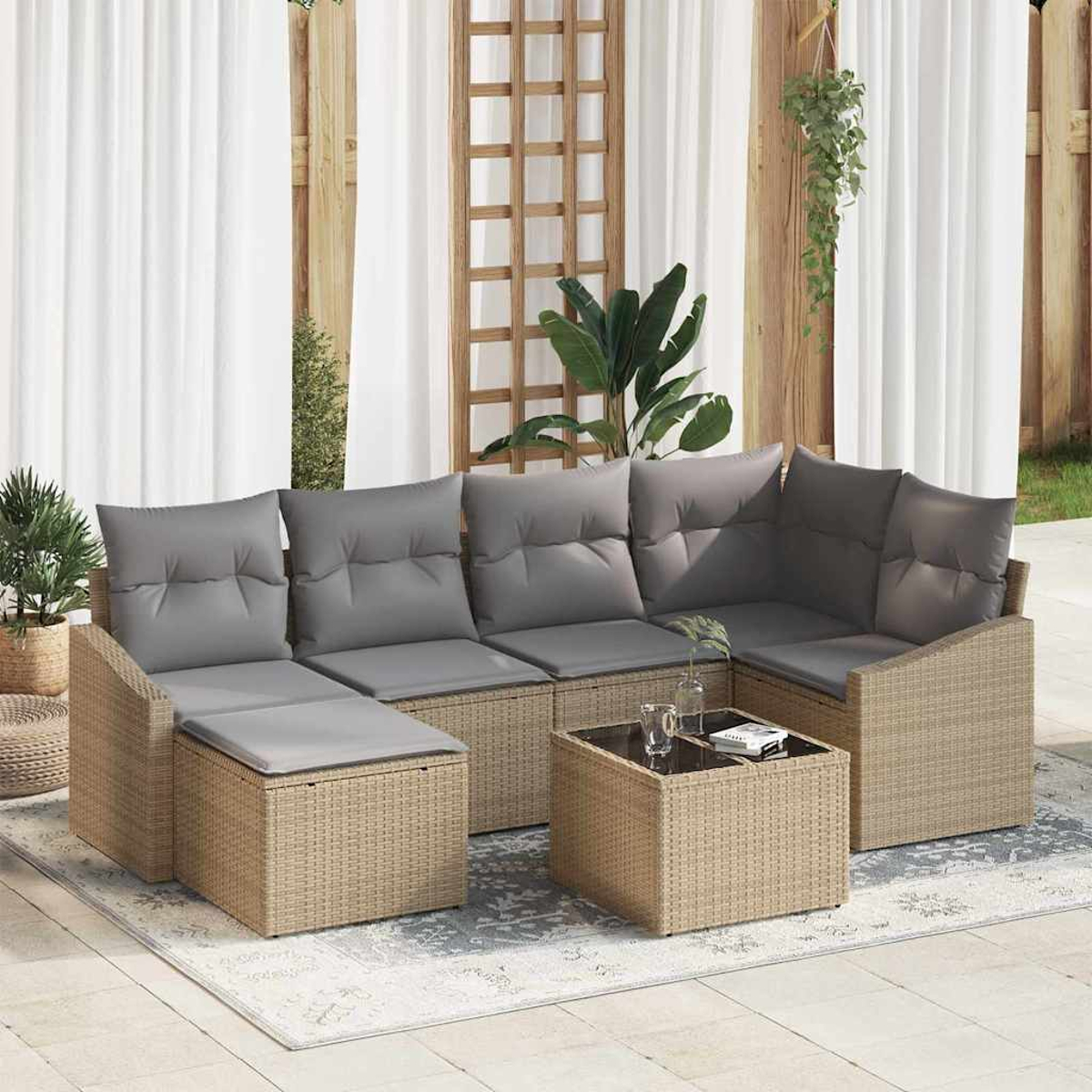 Outdoor-Rattansofa mit grauen Kissen, einem kleinen Tisch mit Gläsern und Pflanzen vor weißem Vorhang.