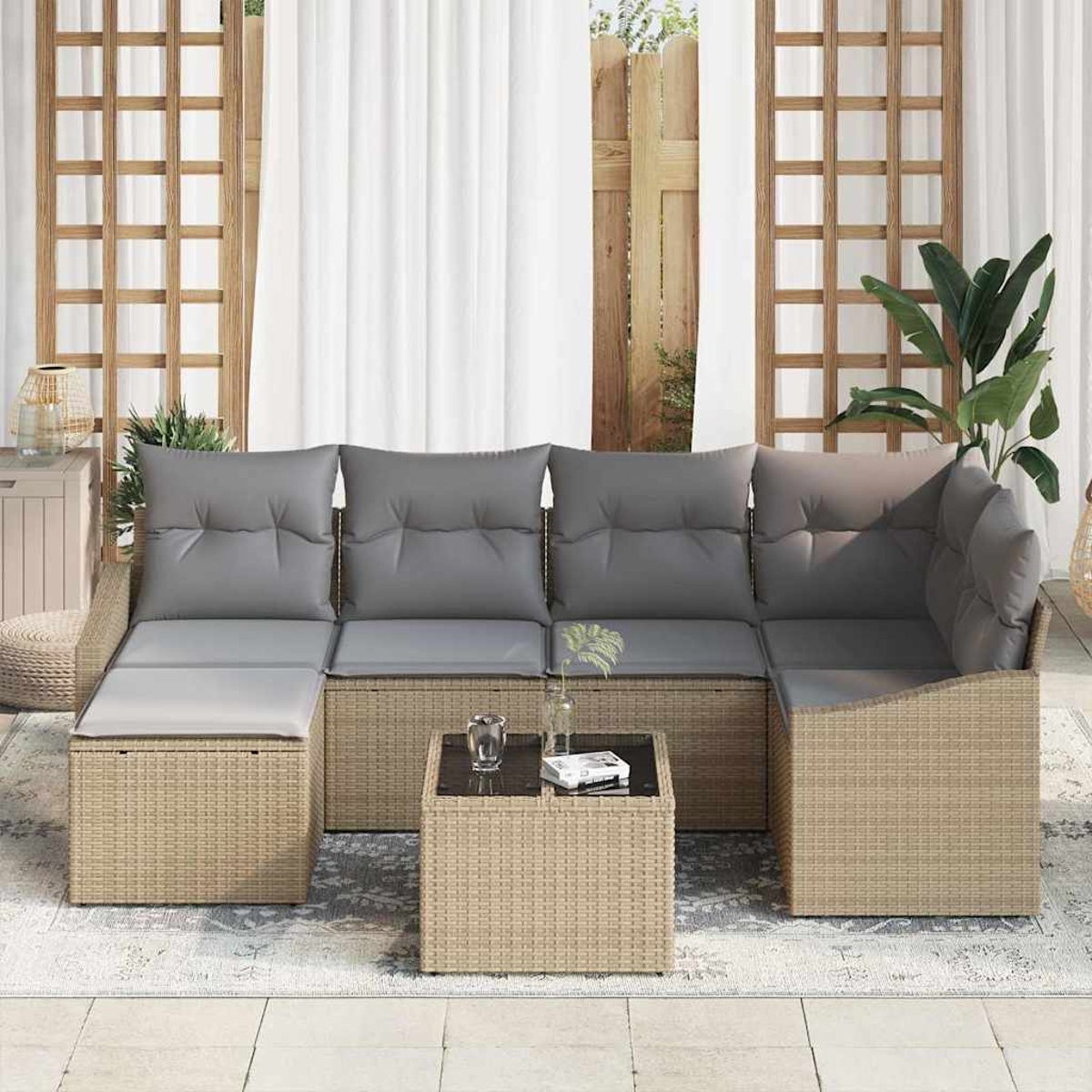 Outdoor-Rattan-Sofa mit grauen Kissen, kleinem Tisch und Teppich. Dahinter Vorhänge und Holzgitter.