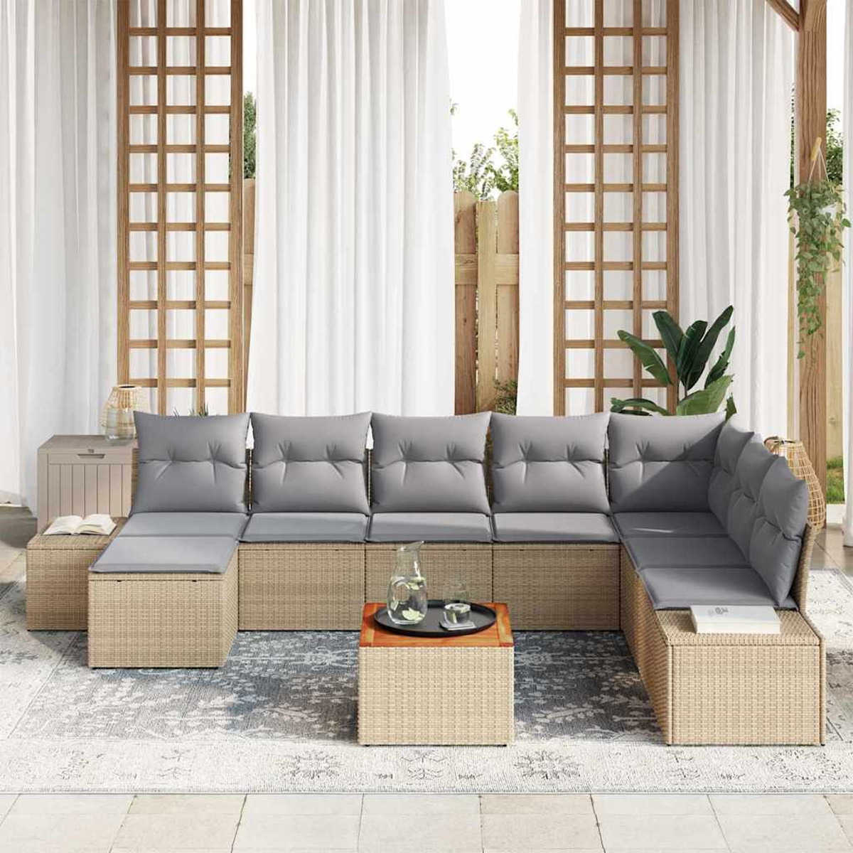 Outdoor-Ecksofa mit grauen Kissen. Geflochtene Rattanbasis, hölzerner Beistelltisch mit Glaskrug und Tablett, weiße Vorhänge im Hintergrund.