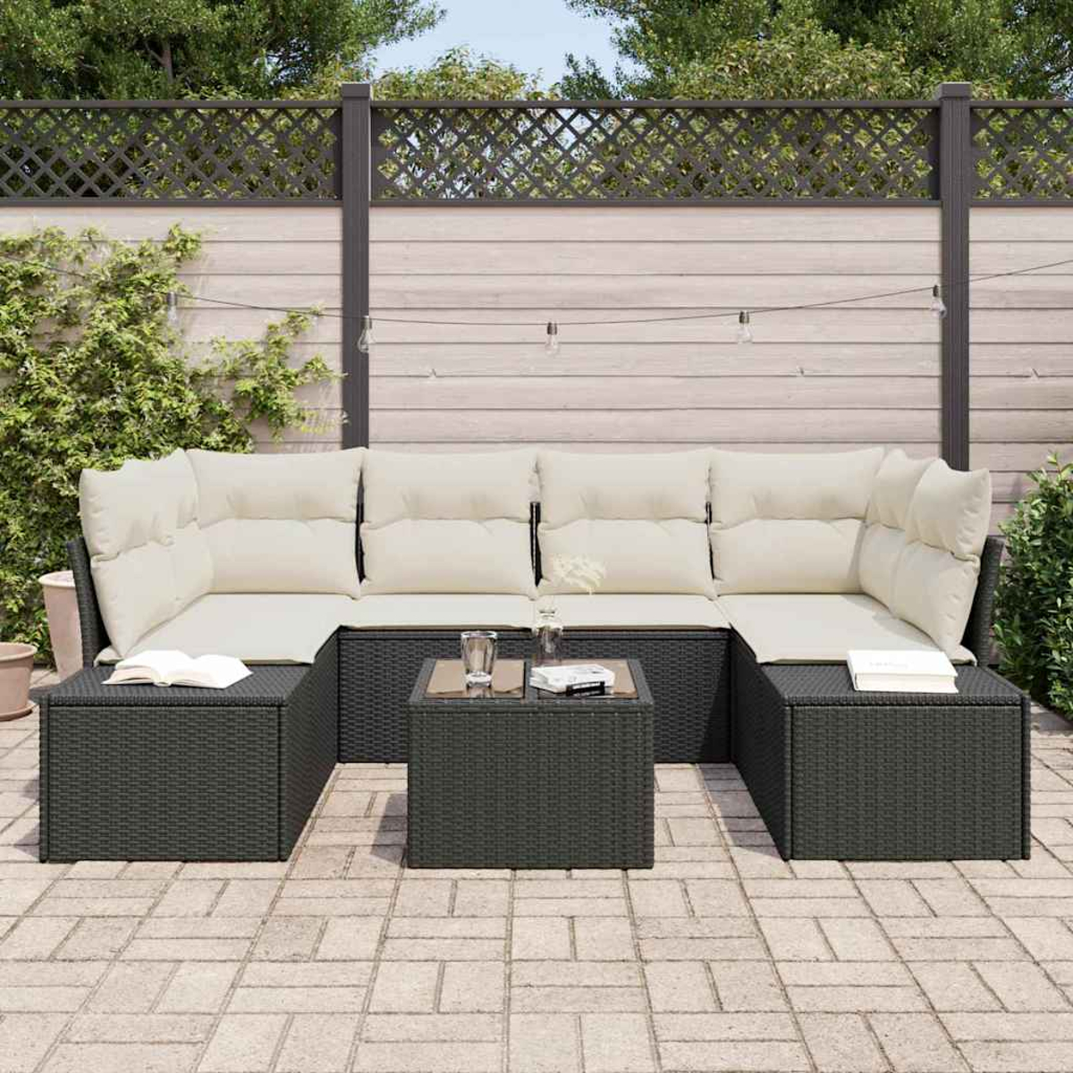 Outdoor-Ecksofa mit cremefarbenen Kissen. Ein Glastisch mit Gläsern und Büchern an der Seite. Holzzaun im Hintergrund.