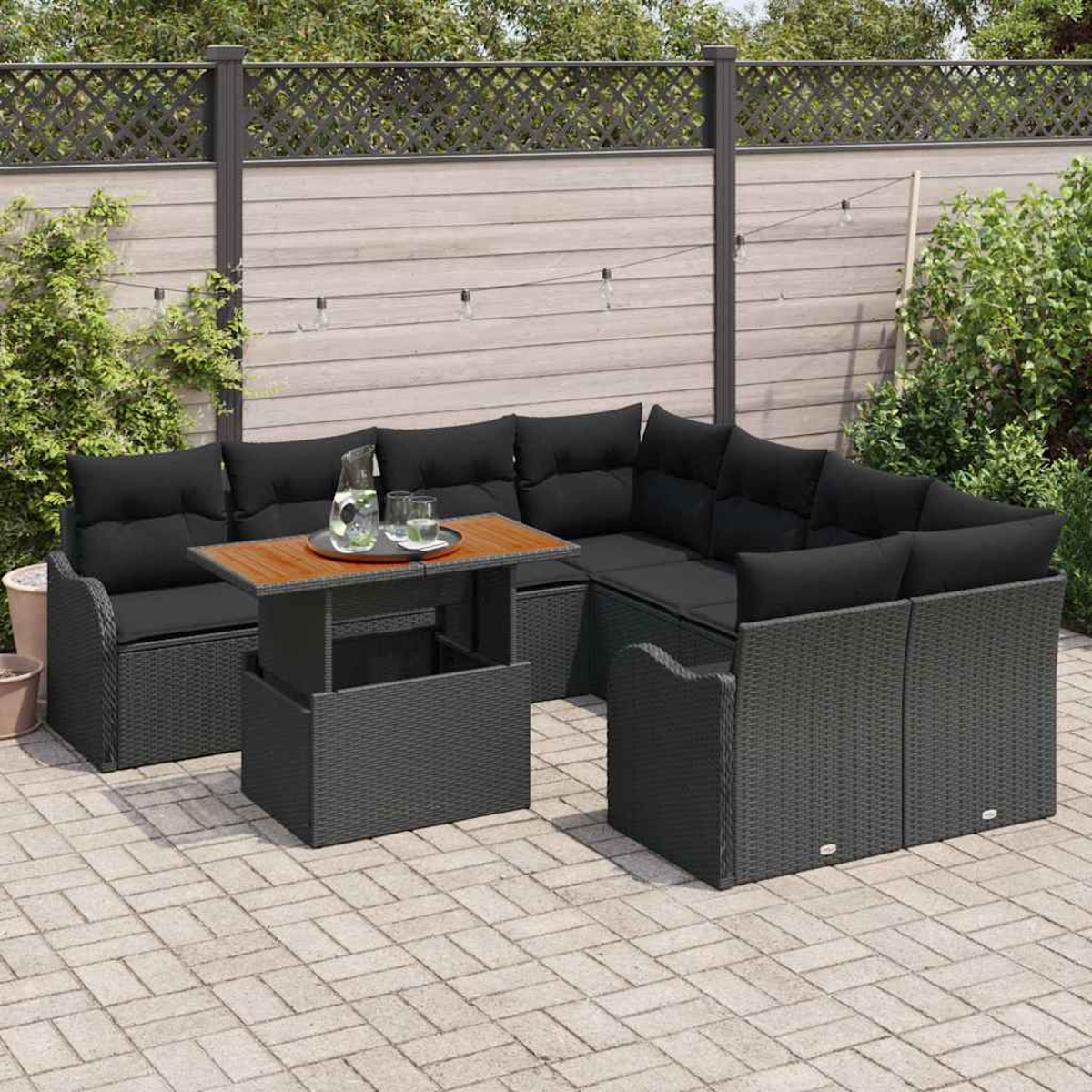Outdoor-Ecksofa mit schwarzen Kissen, Holztisch mit Getränken, auf Steinterrasse, umgeben von Grün und einem Zaun.