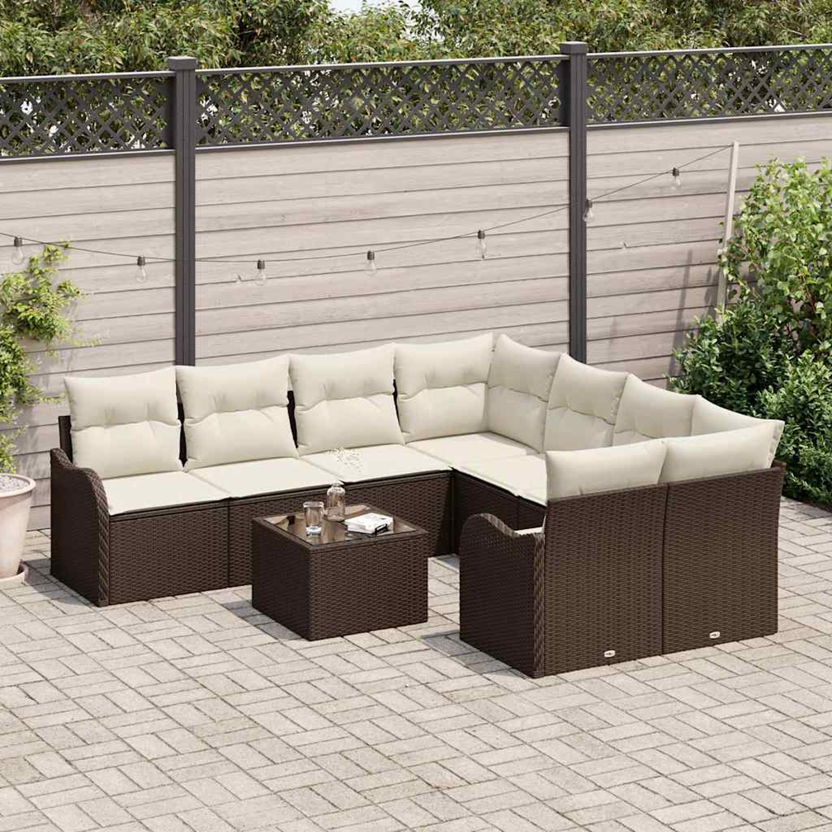 Garten-Sitzgruppe mit braunem Korbgeflecht und cremefarbenen Kissen auf einer Steinterrasse. Ein kleiner Tisch mit Gläsern. Holzzaun im Hintergrund.
