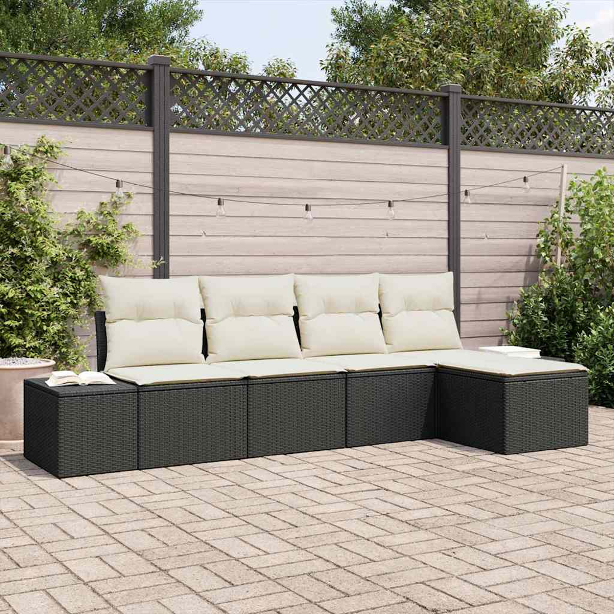 Outdoor-Ecksofa mit cremefarbenen Kissen. Dunkelgraue Korbmöbel auf einer Ziegelterrasse. Holzzaun und Grün im Hintergrund.