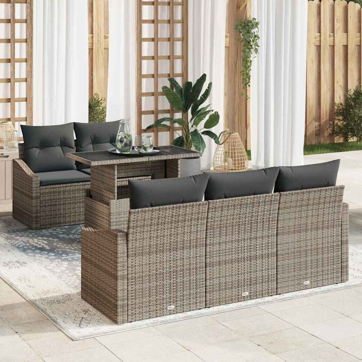 Rattan-Terrassenmöbel-Set mit grauen Kissen, Tisch und Sofa. Weiße Vorhänge und Holzzaun im Hintergrund.