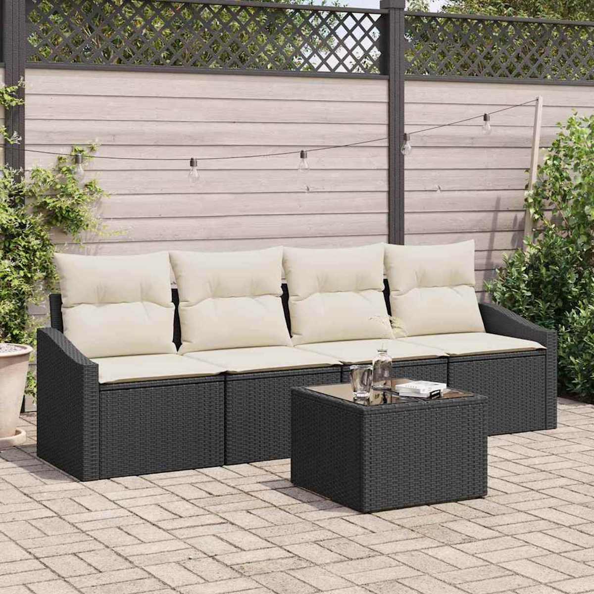 Dunkelgraues Rattansofa mit cremefarbenen Kissen und einem quadratischen Couchtisch. Auf einer Steinterrasse, mit Grün im Hintergrund.