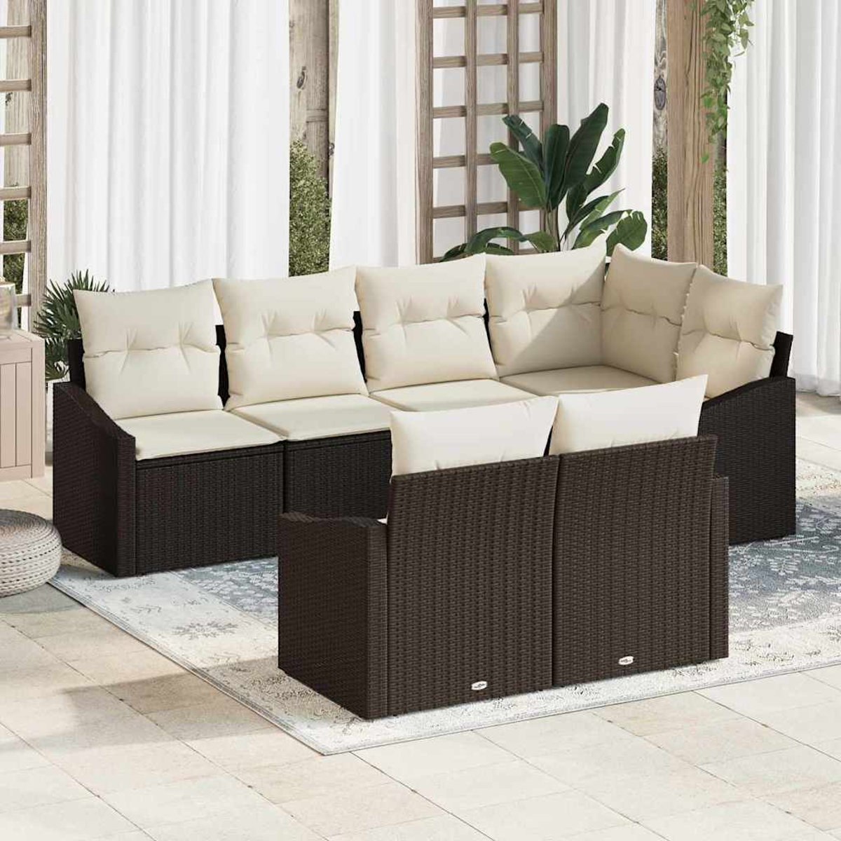 Garten-Wicker-Sofagarnitur mit cremefarbenen Kissen. Weiße Vorhänge und ein Spalier im Hintergrund. Ein Teppich auf der Terrasse.