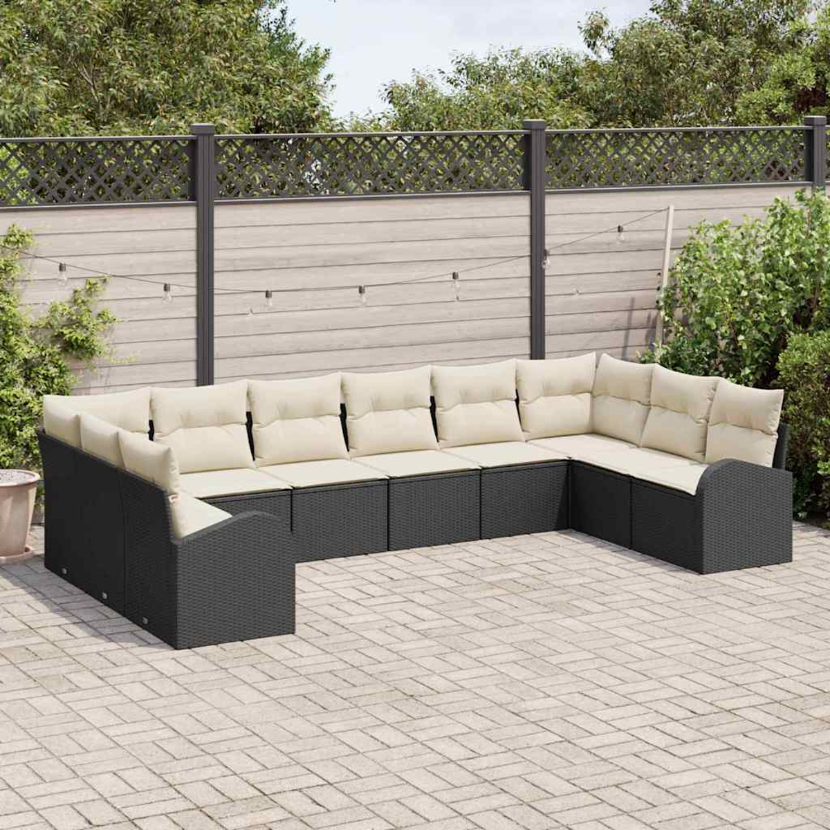 Ein schwarzes Ecksofa mit cremefarbenen Kissen steht auf einer gepflasterten Terrasse. Im Hintergrund befindet sich ein Holzzaun mit Grün.