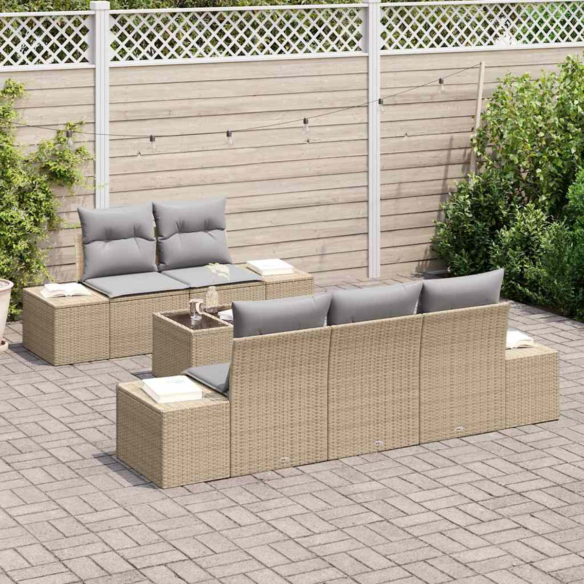 Gartenmöbel-Set aus beigem Korbgeflecht und grauen Kissen. Enthält ein Sofa, eine Couch und kleine Tische auf einer Ziegelterrasse mit Zaun.