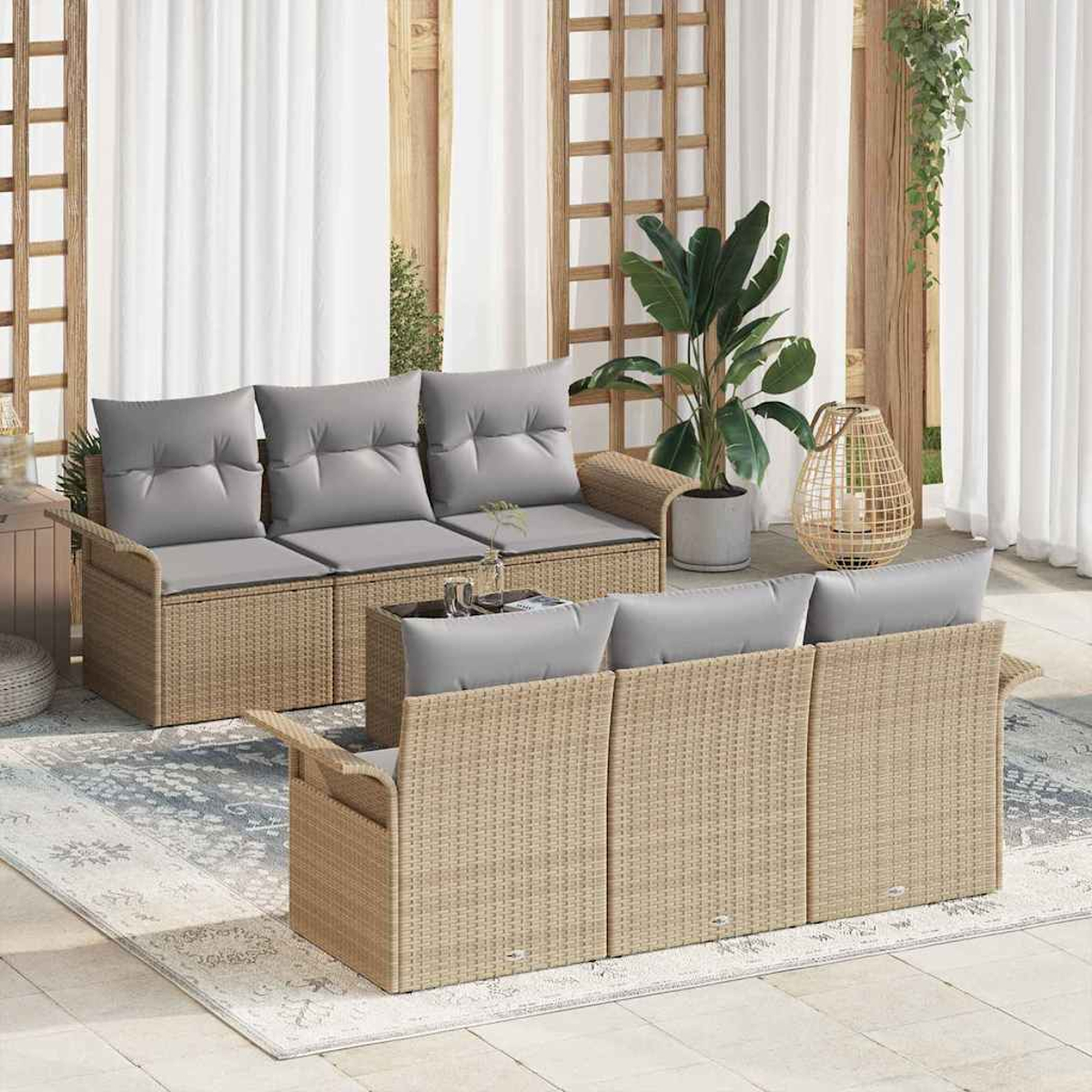 Gartenmöbel-Set mit gewebten Rahmen im Rattan-Stil, grauen Kissen und einem Tisch mit Glasplatte. Im Hintergrund Pflanzen und ein Teppich.