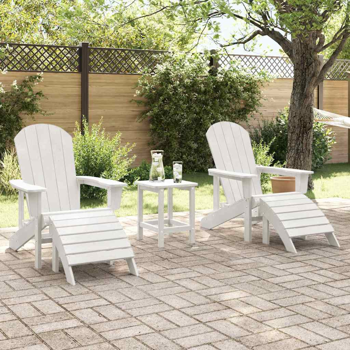 Weiße Adirondack-Stühle und Fußstützen auf einer Ziegelterrasse. Ein kleiner Tisch mit Getränken steht zwischen den Stühlen. Grünes Laub im Hintergrund.