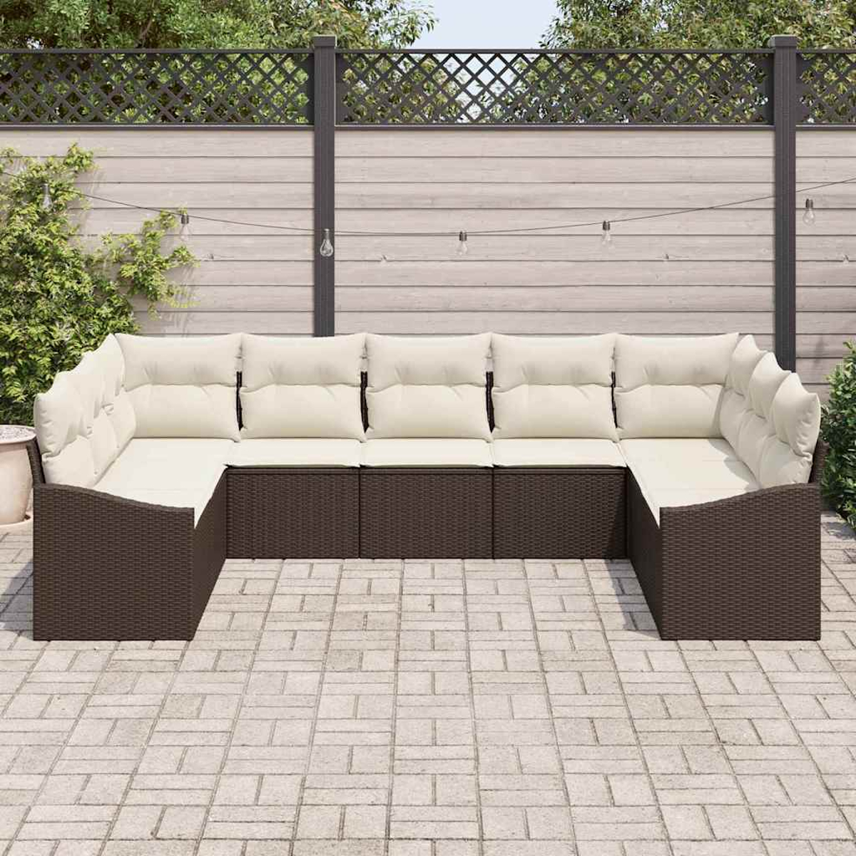 U-förmiges Outdoor-Sofa mit cremefarbenen Kissen, braunem Korbgewebe, auf einer Ziegelpflasterterrasse. Zaun und Grün im Hintergrund.