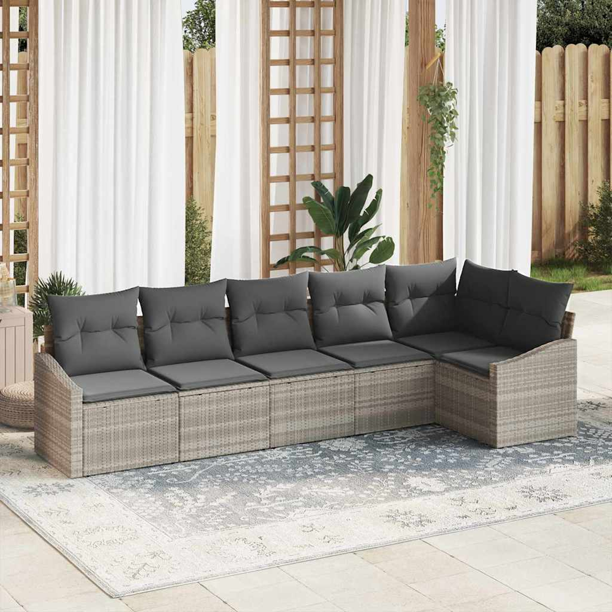 Ein Ecksofa mit grauen Kissen steht auf einem gemusterten Teppich. Weiße Vorhänge und ein Holzzaun sind im Hintergrund zu sehen.