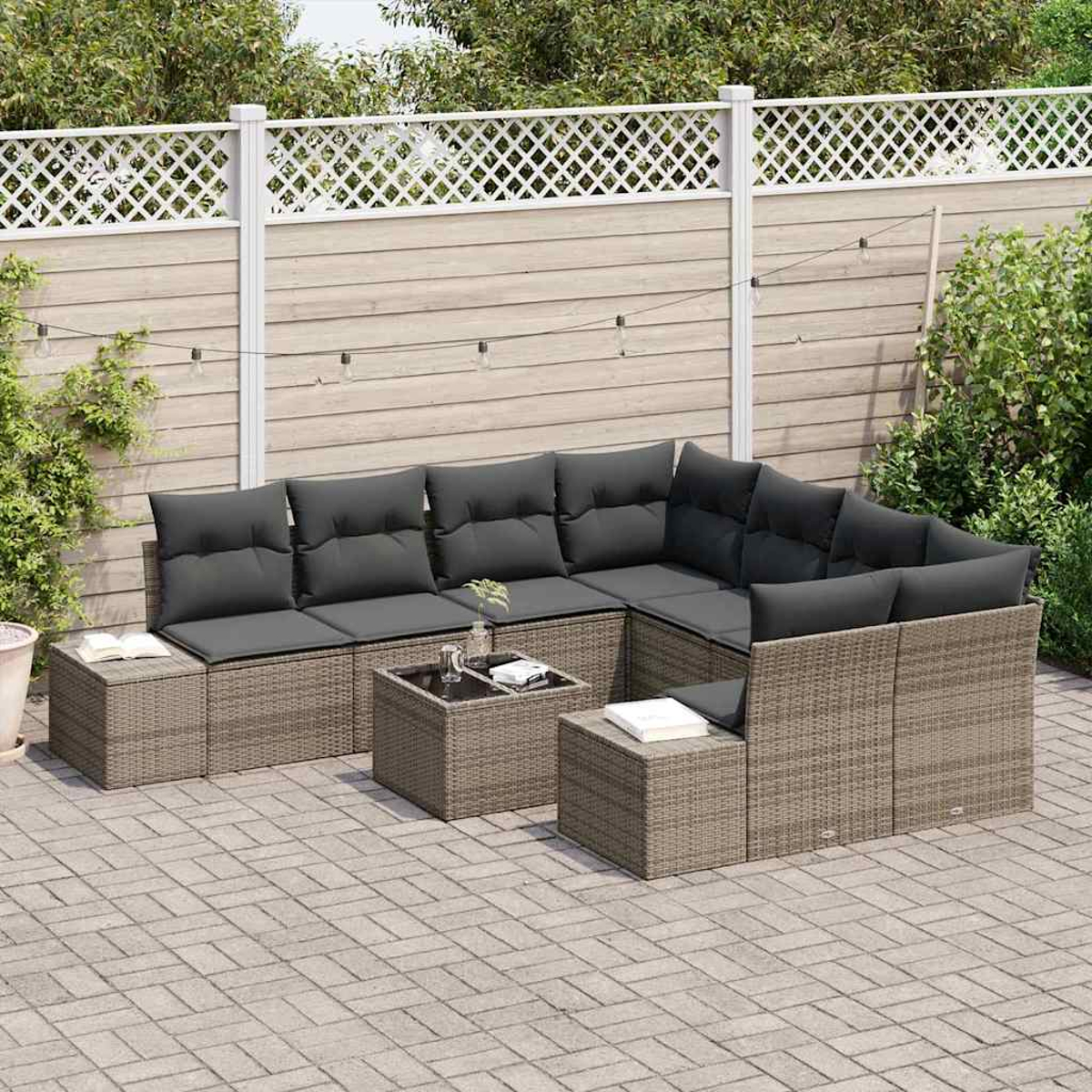 Sofá seccional exterior con cojines grises. Dos mesas cuadradas y una rectangular. Valla blanca y plantas en el fondo.