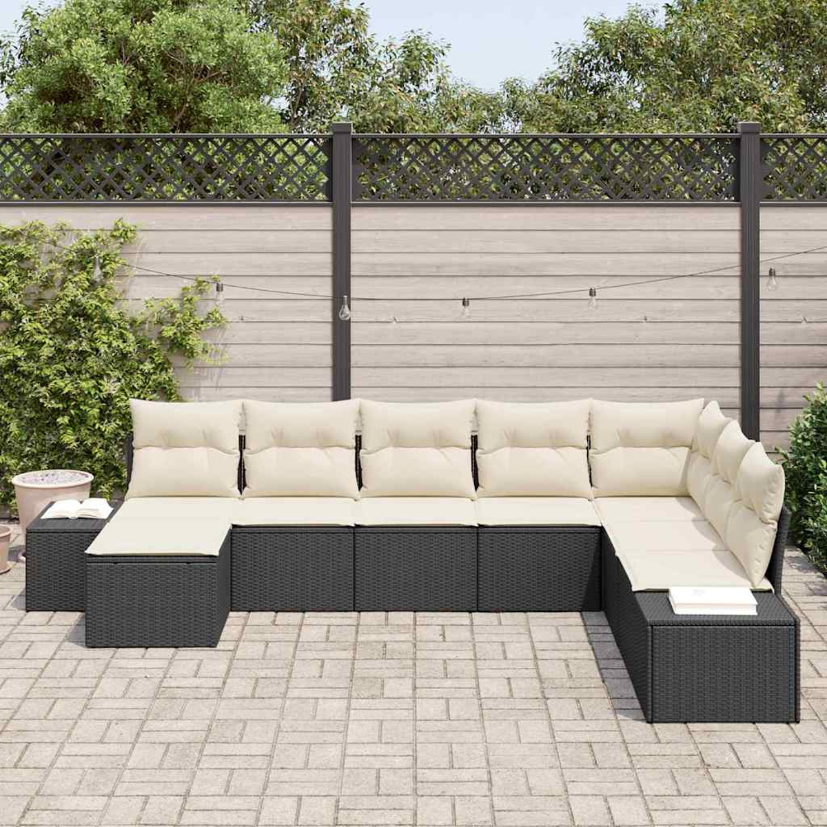 Dunkelgraues Ecksofa mit cremefarbenen Kissen auf einer Terrasse. Dahinter ein Holzzaun und Grün.