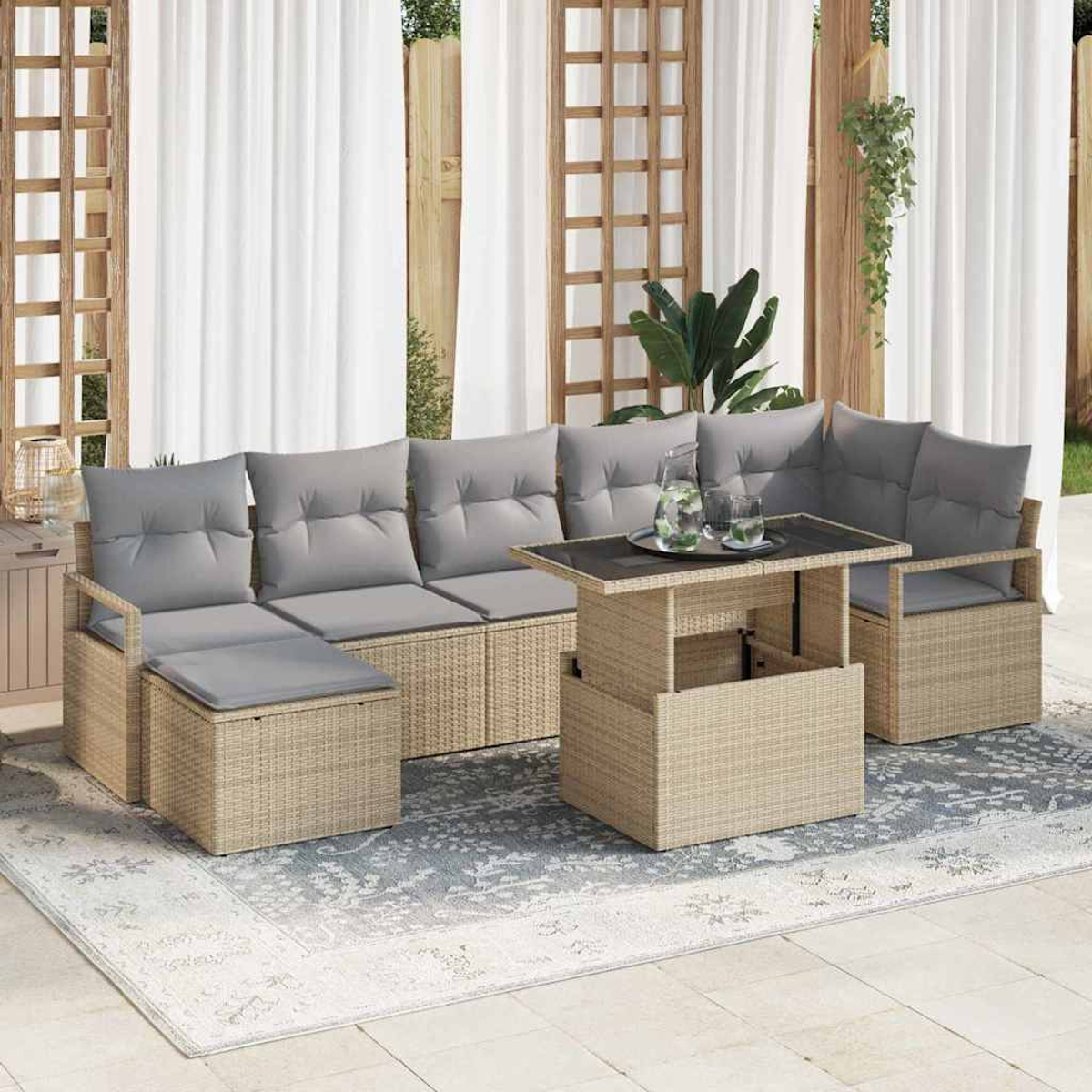 Sof á seccional de mimbre para exteriores con cojines grises y una mesa elevable. Cortinas blancas y enrejado de madera al fondo. Una alfombra estampada.