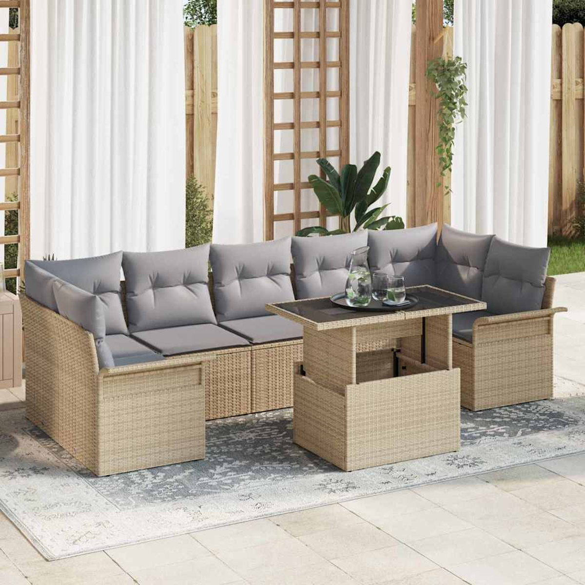 Garten-Korbmöbel-Set mit grauen Kissen und einem Tisch mit Hubfunktion auf einem gemusterten Teppich. Weiße Vorhänge und Holzgitter im Hintergrund.