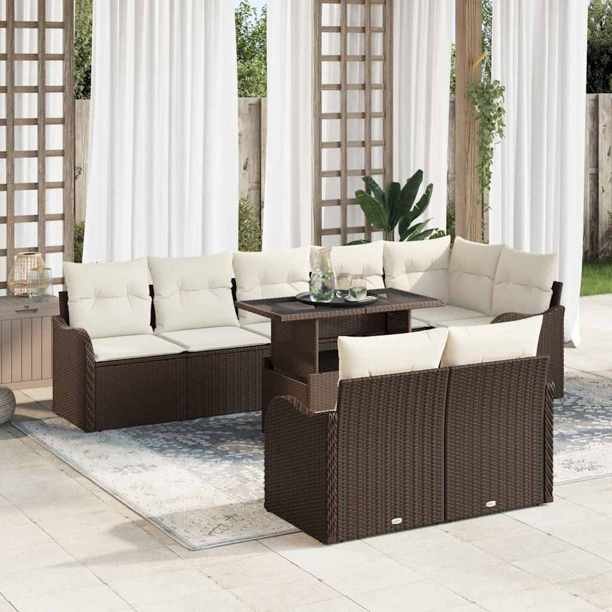 Garten-Terrassenset mit braunen Korbmöbeln, cremefarbenen Kissen und einem Tisch mit Glasplatte. Weiße Vorhänge und Grün im Hintergrund.