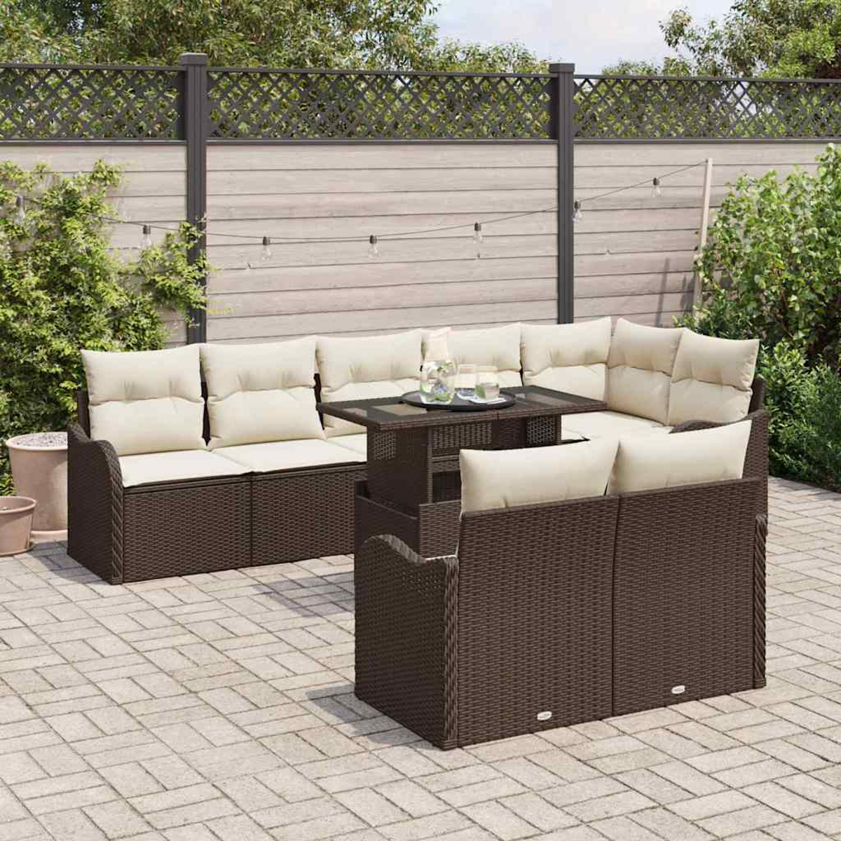 Outdoor-Terrassenset mit braunen Korbmöbeln, cremefarbenen Kissen und einem Tisch mit Glasplatte. Auf einer Backsteinterrasse mit Holzzaun.