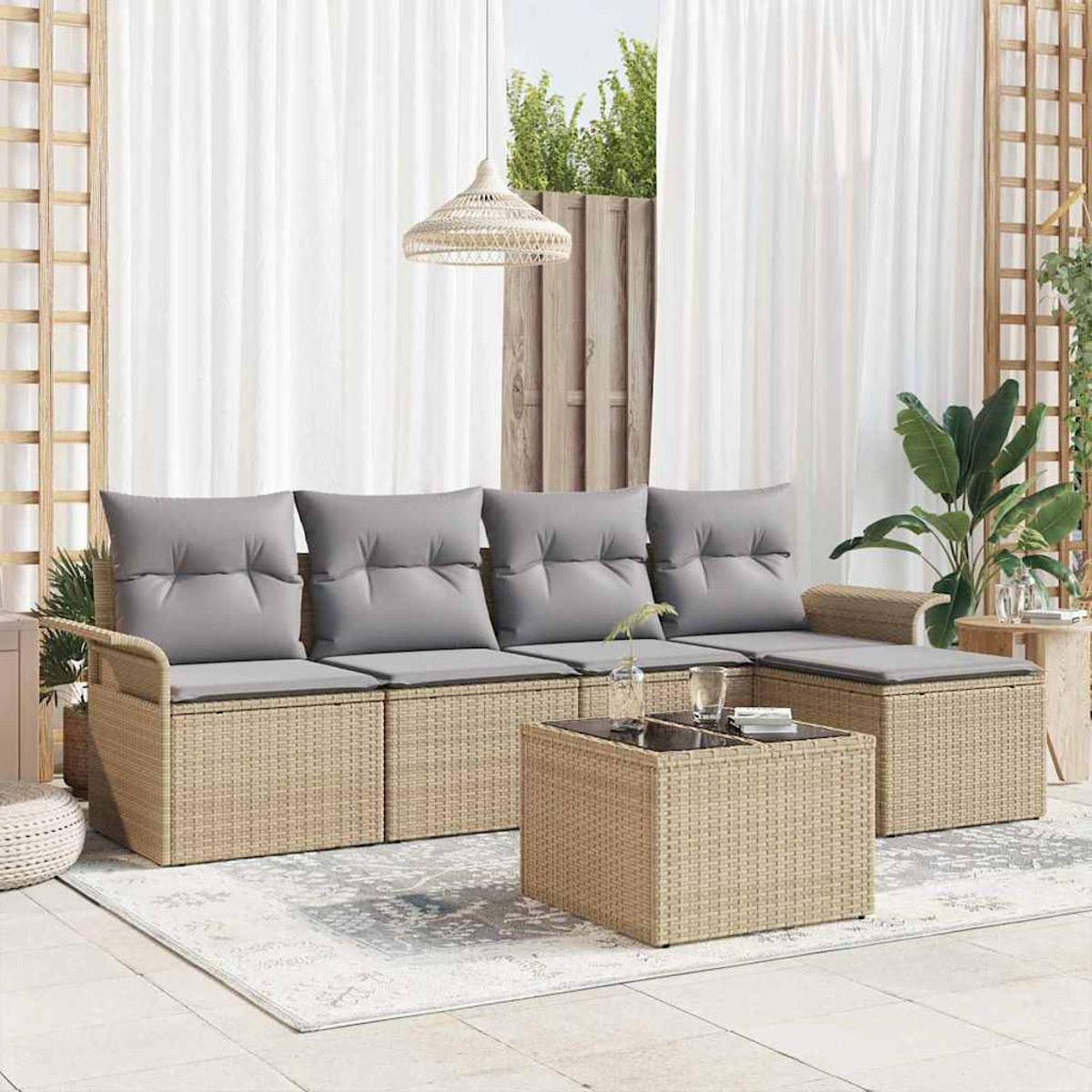 Outdoor-Sitzbereich mit Rattansofa, grauen Kissen, Glastisch und weißen Vorhängen. Pflanzen und eine gewebte Lampe vervollständigen die Szene.