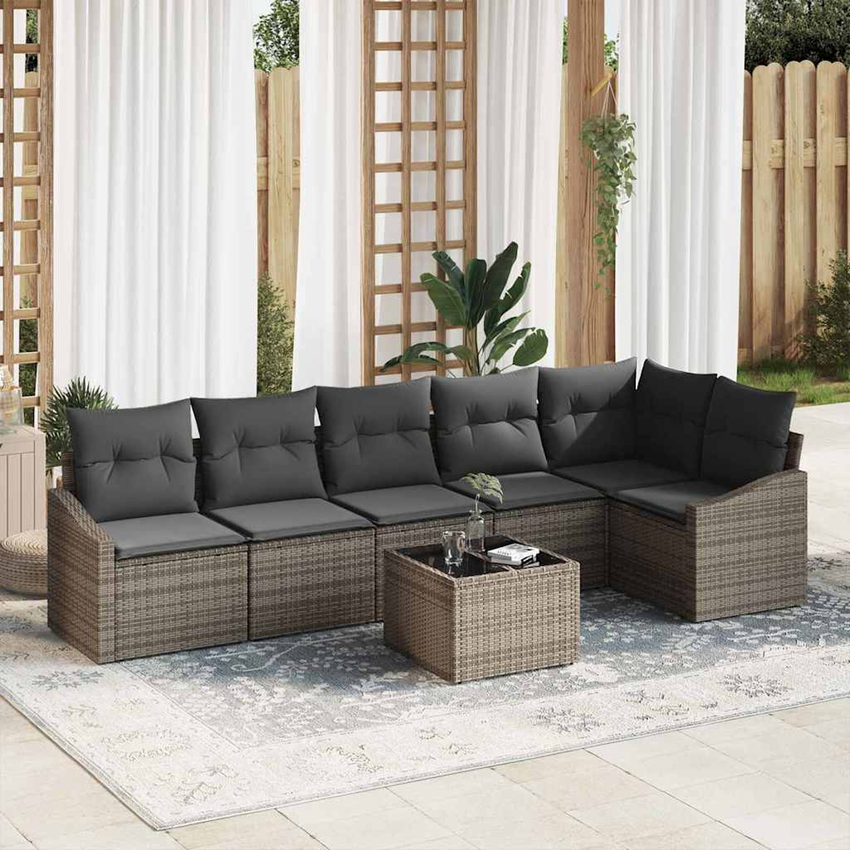Ein graues Outdoor-Ecksofa mit dunklen Kissen und einem passenden Couchtisch steht auf einem Teppich in einer Terrasse, mit Vorhängen dahinter.