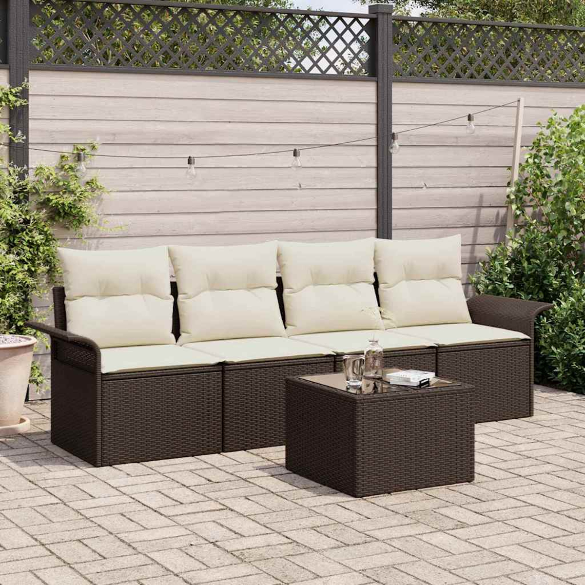 Garten-Set mit braunem Korbmöbel-Sofa, cremefarbenen Kissen und einem passenden Couchtisch. Im Hintergrund ein Holzzaun.