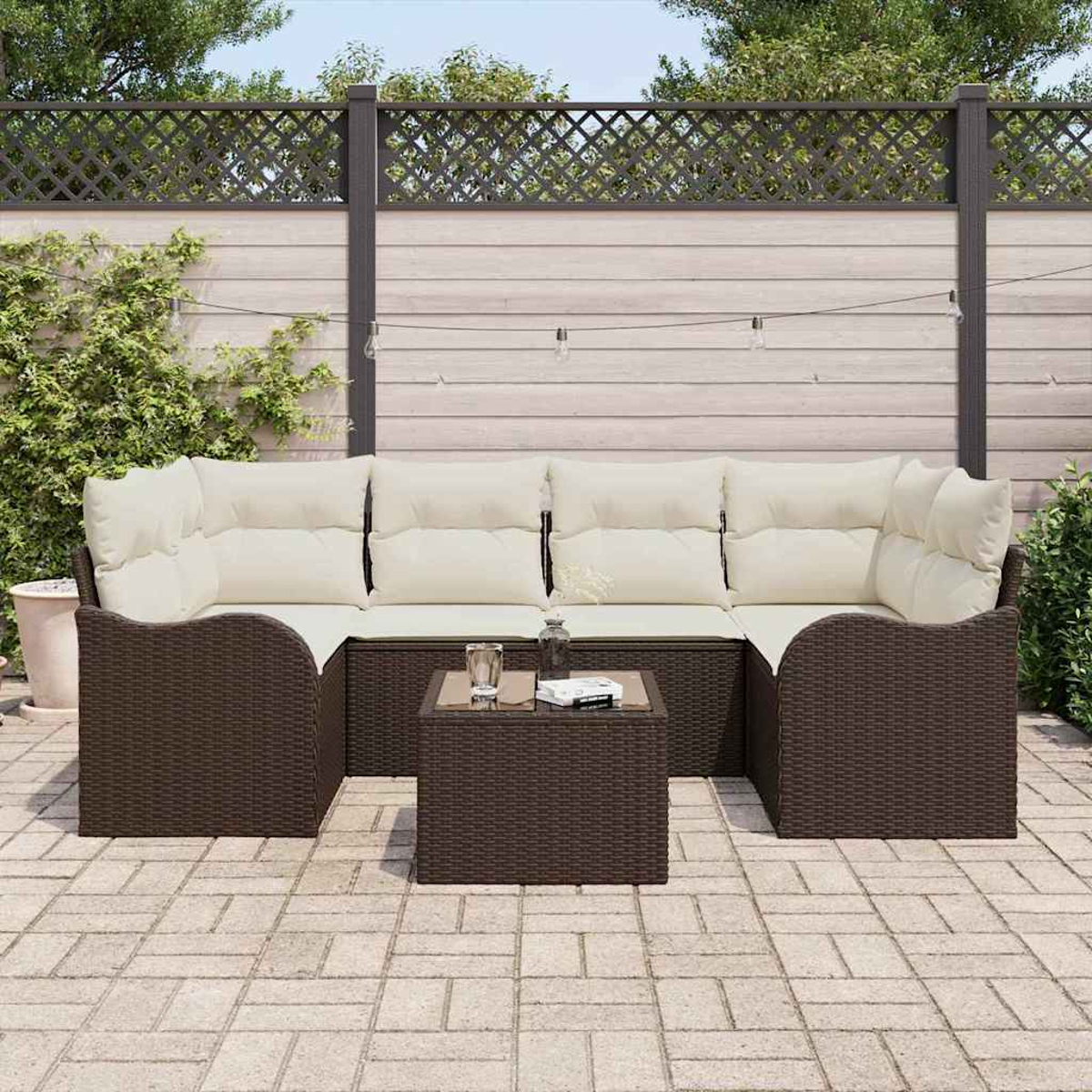 Garten-Sitzgruppe: braunes Korbmöbel mit cremefarbenen Kissen und kleinem quadratischem Tisch auf Steinplatten.