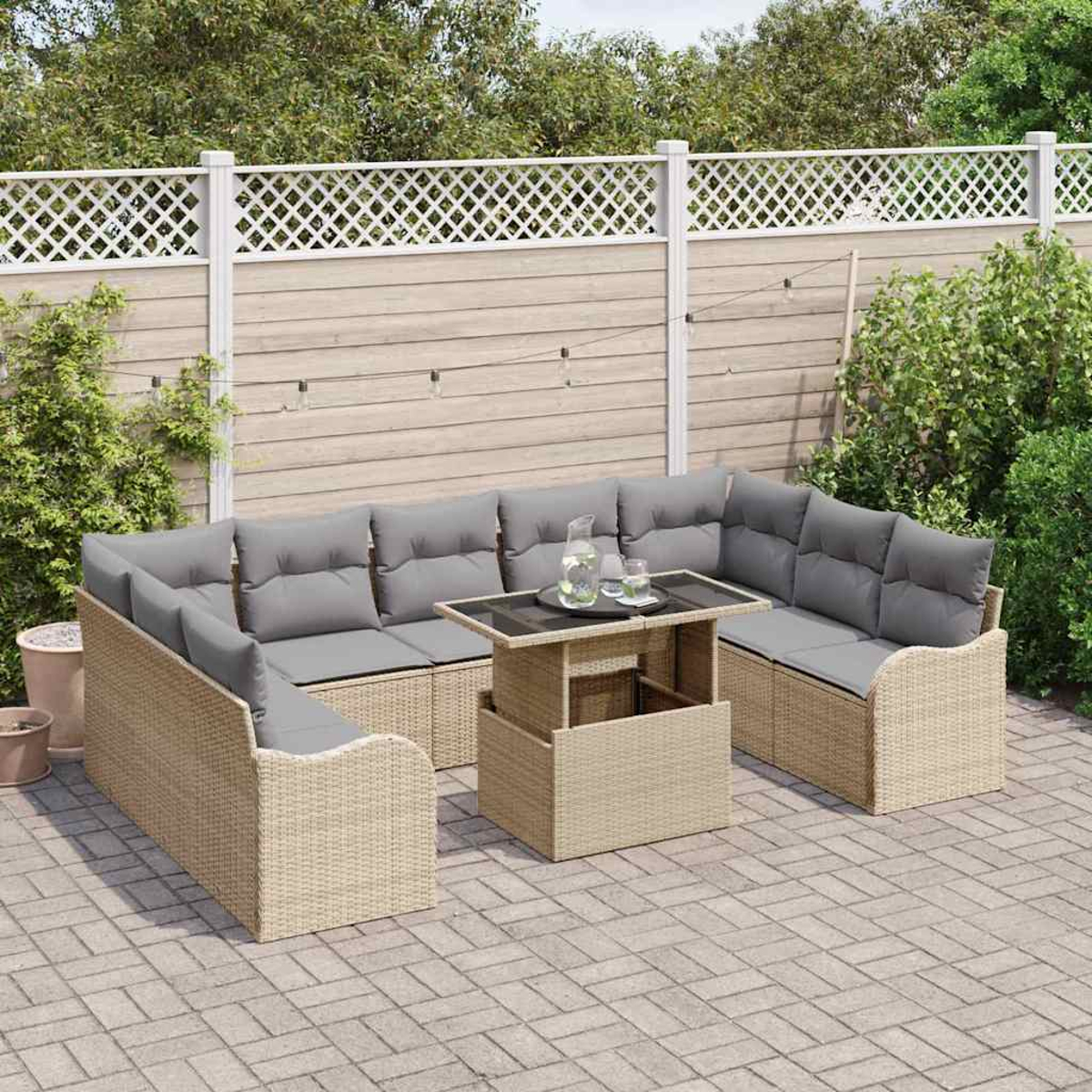 Garten-Terrassenset mit beigen Korbmöbeln, grauen Kissen und einem Tisch mit Hubfunktion. Vor einem Zaun und Grün.