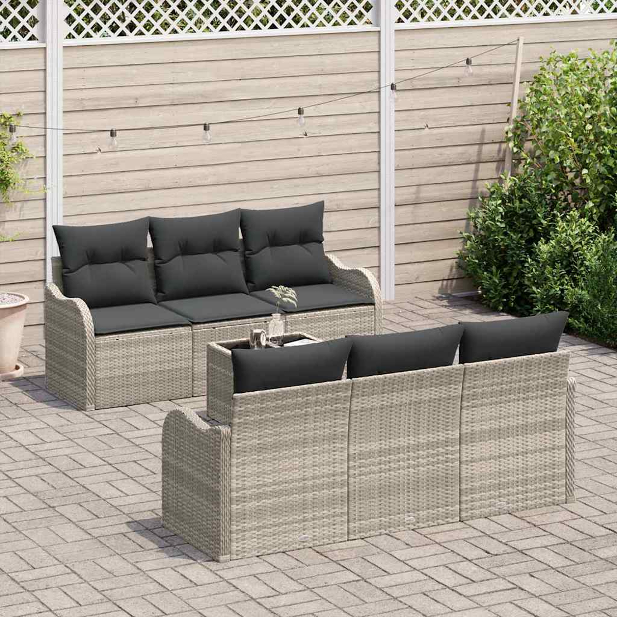 Gartenmöbel-Set mit grauen Kissen. Zwei Rattansofas und ein Couchtisch auf einer Ziegelterrasse. Im Hintergrund ein Holzzaun.