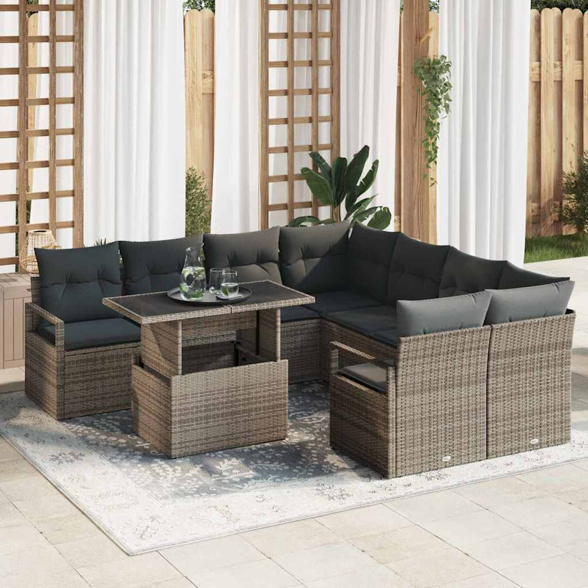 Garten-Sitzgruppe auf einem Teppich. Sie beinhaltet einen Tisch mit Gläsern und einer Wasserkaraffe sowie ein Ecksofa mit dunklen Kissen.