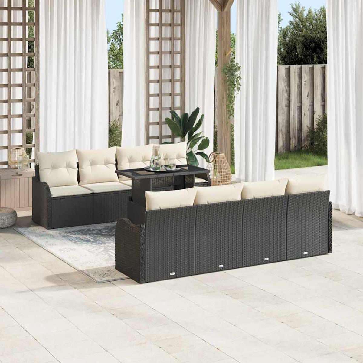 Garten-Set mit grauen Korbmöbeln, cremefarbenen Kissen und einem Tisch mit Glasplatte. Weiße Vorhänge und Holzgitter im Hintergrund.