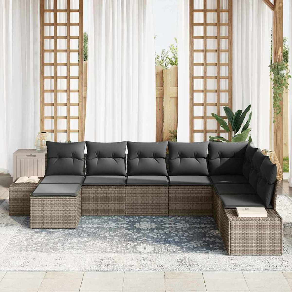 Outdoor-Ecksofa mit grauen Kissen auf einem blauen Teppich. Weiße Vorhänge, Holzgitter und Pflanzen im Hintergrund.